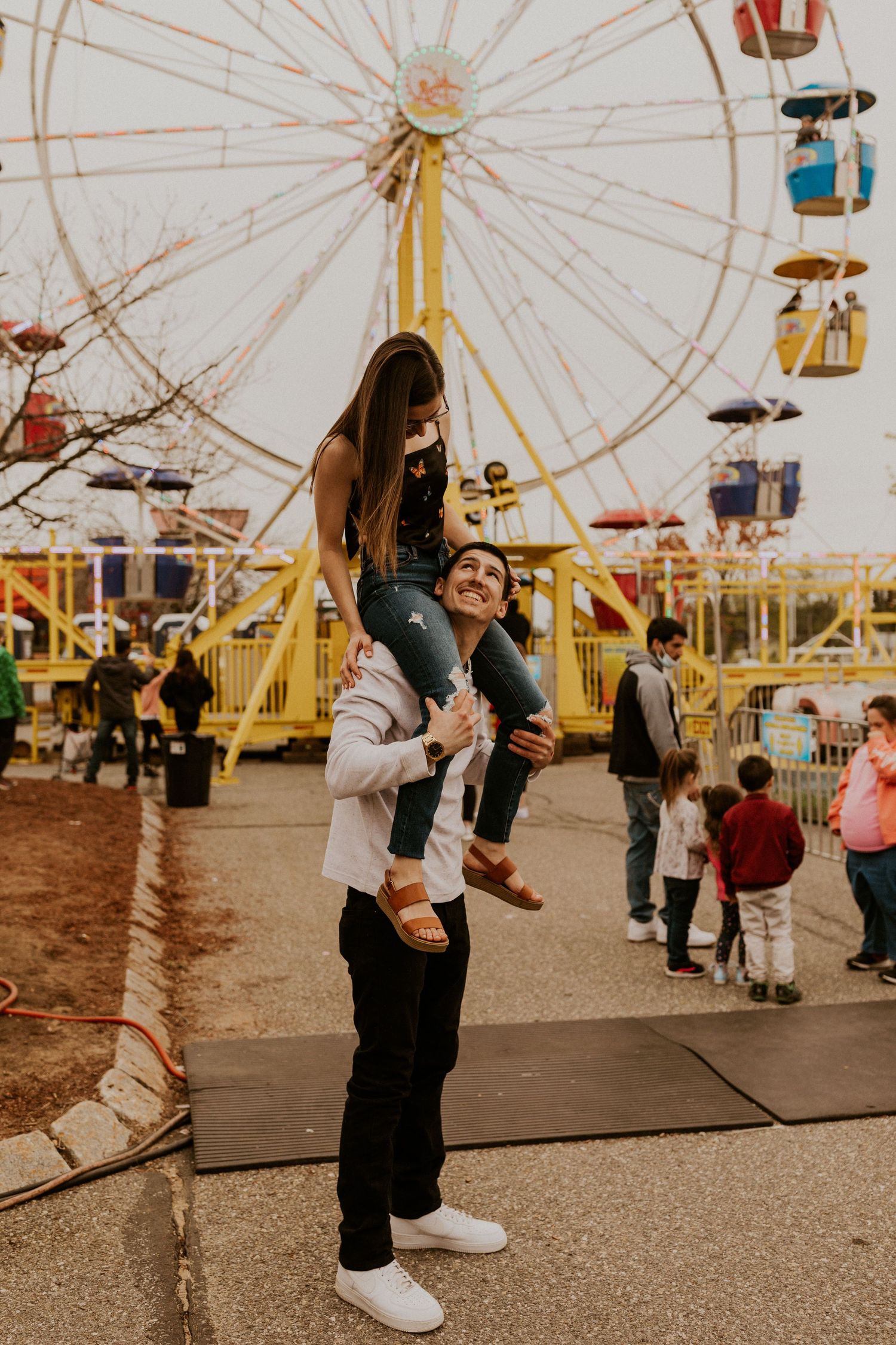 Playful couple dancing together at a carnival with a ferris wheel in the background.
