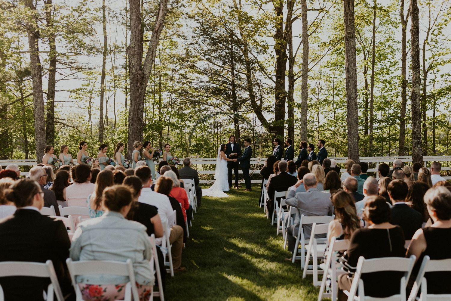 Chrissy and Mike holding hands as their wedding ceremony begins. It is a lovely spring day with the sun shining.