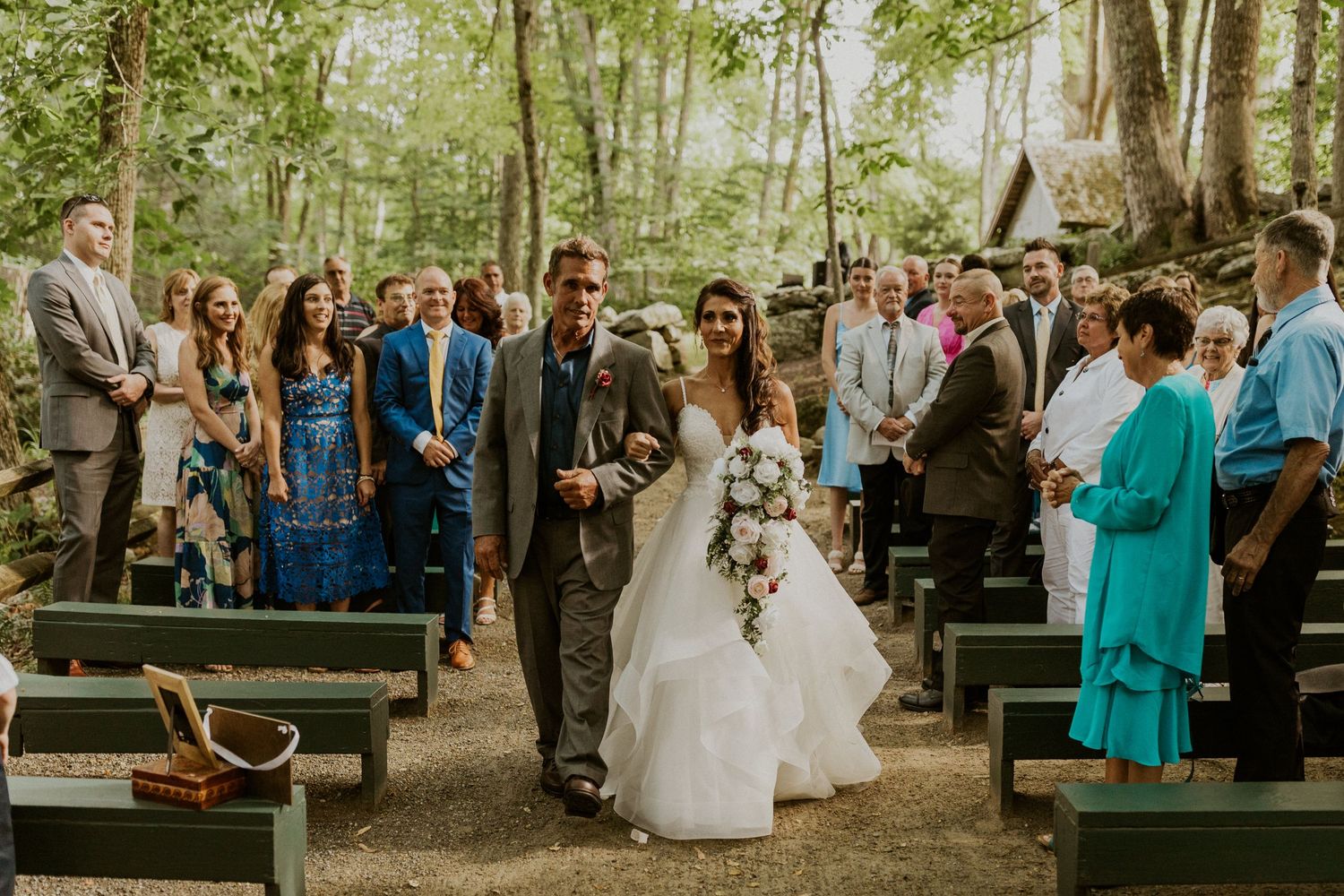Wedding ceremony in a serene forest setting with guests seated on wooden benches.