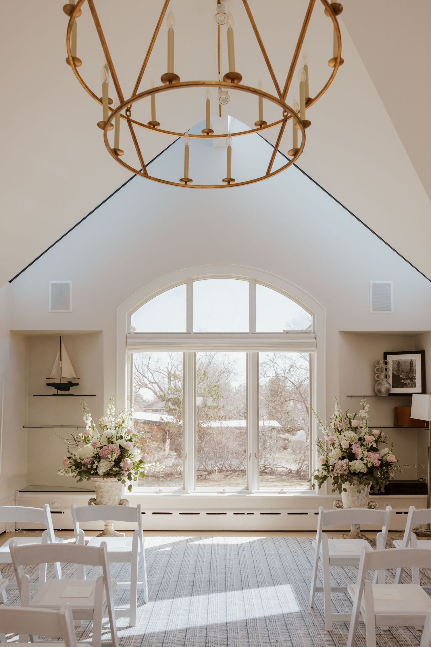 Modern white dining room interior with arched windows, circular chandeliers, and white cross-back chairs in natural light.