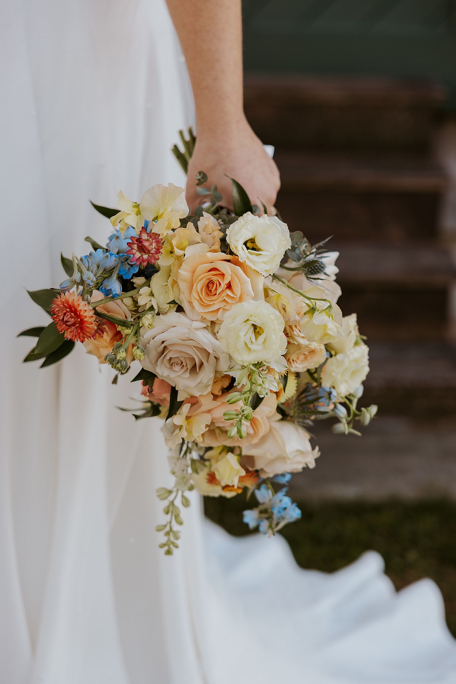 Bride holding a bouquet of peach, organge, cream and blue flowers for her fall New Hampshire wedding
