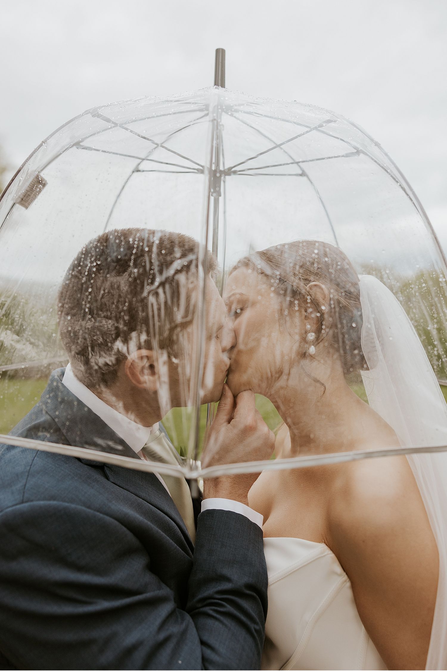 Romantic moment under a clear umbrella on a cloudy wedding day.