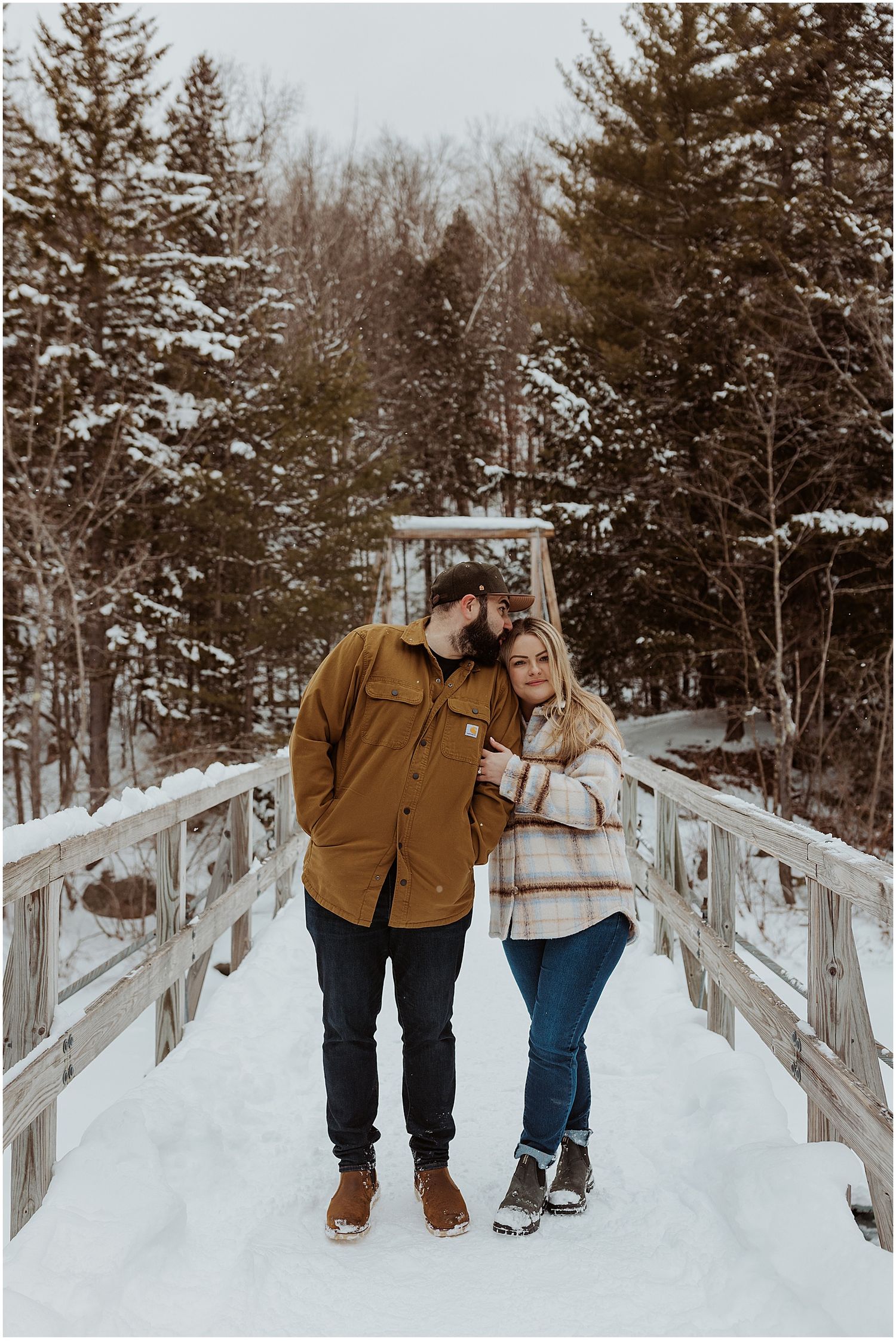 Couple taking winter engagement pictures in the White Mountains wearing winter engagement photo outfits