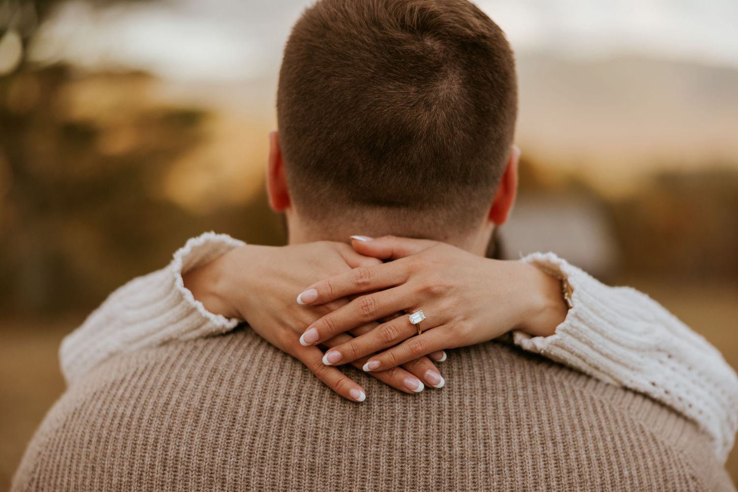 Close-up of a woman's hand with engagement ring resting on man's shoulder.