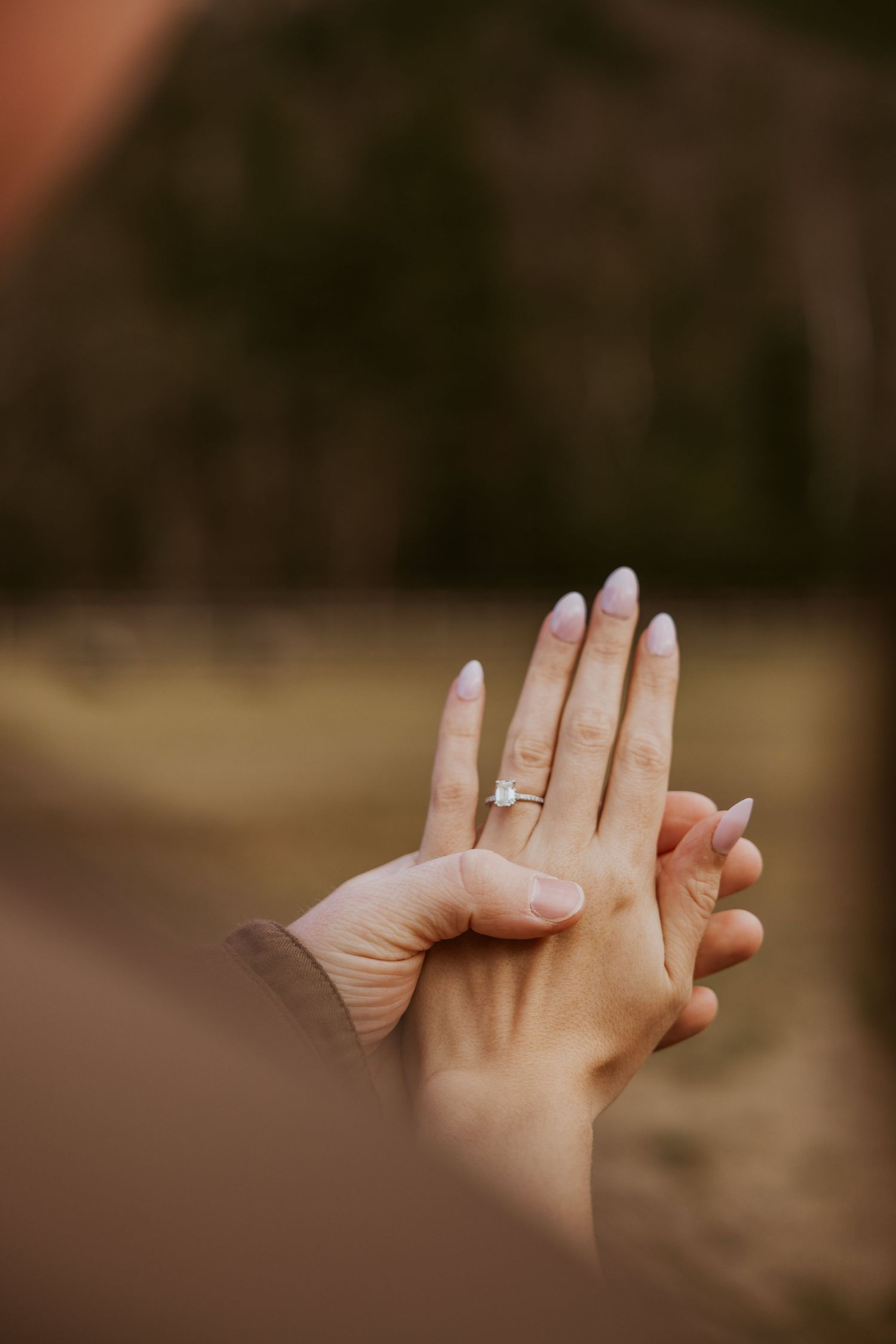 Close-up of an engagement ring on a woman's hand held by her partner outdoors.