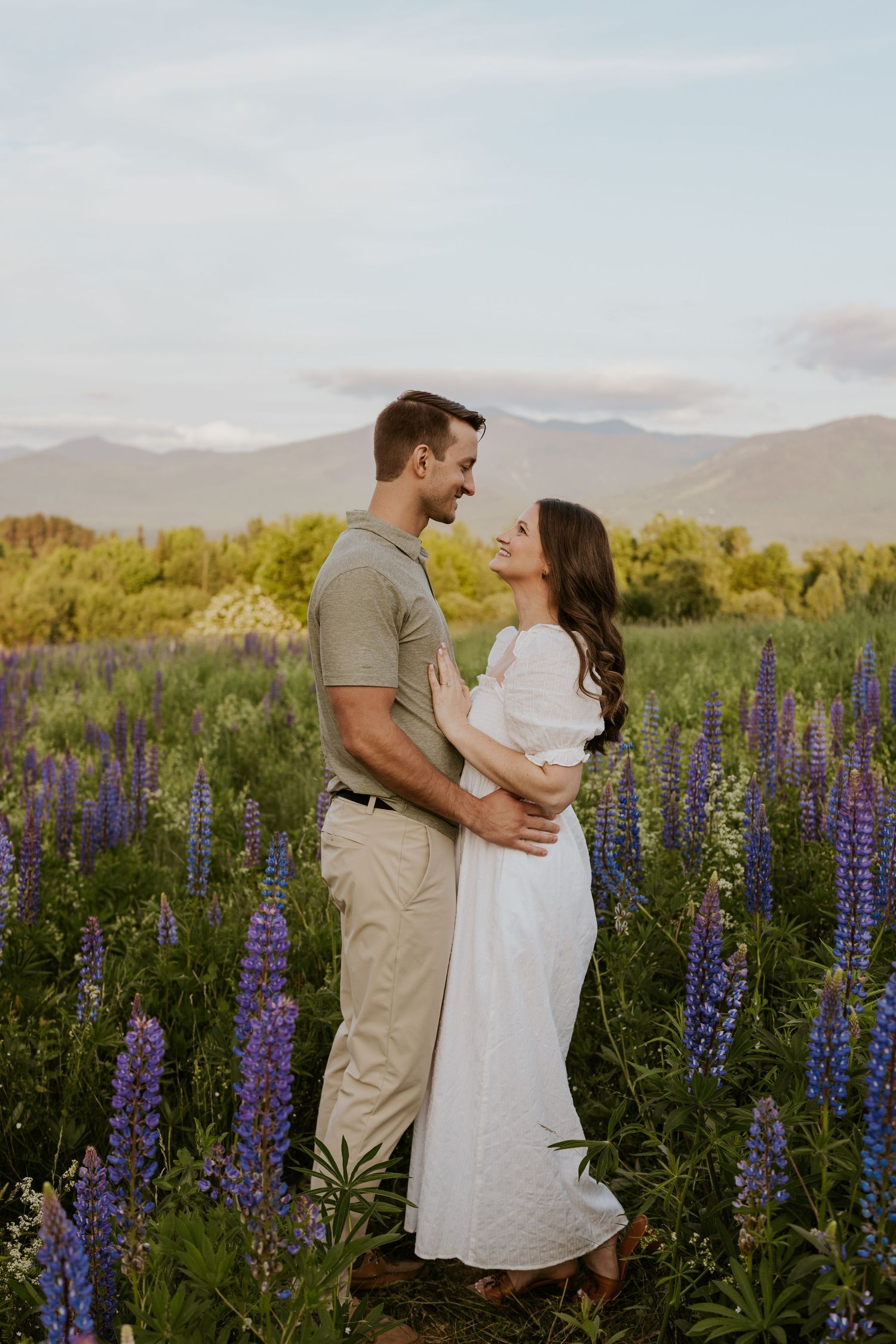 Couple embracing in a stunning purple lupine field with mountain backdrop at golden hour.
