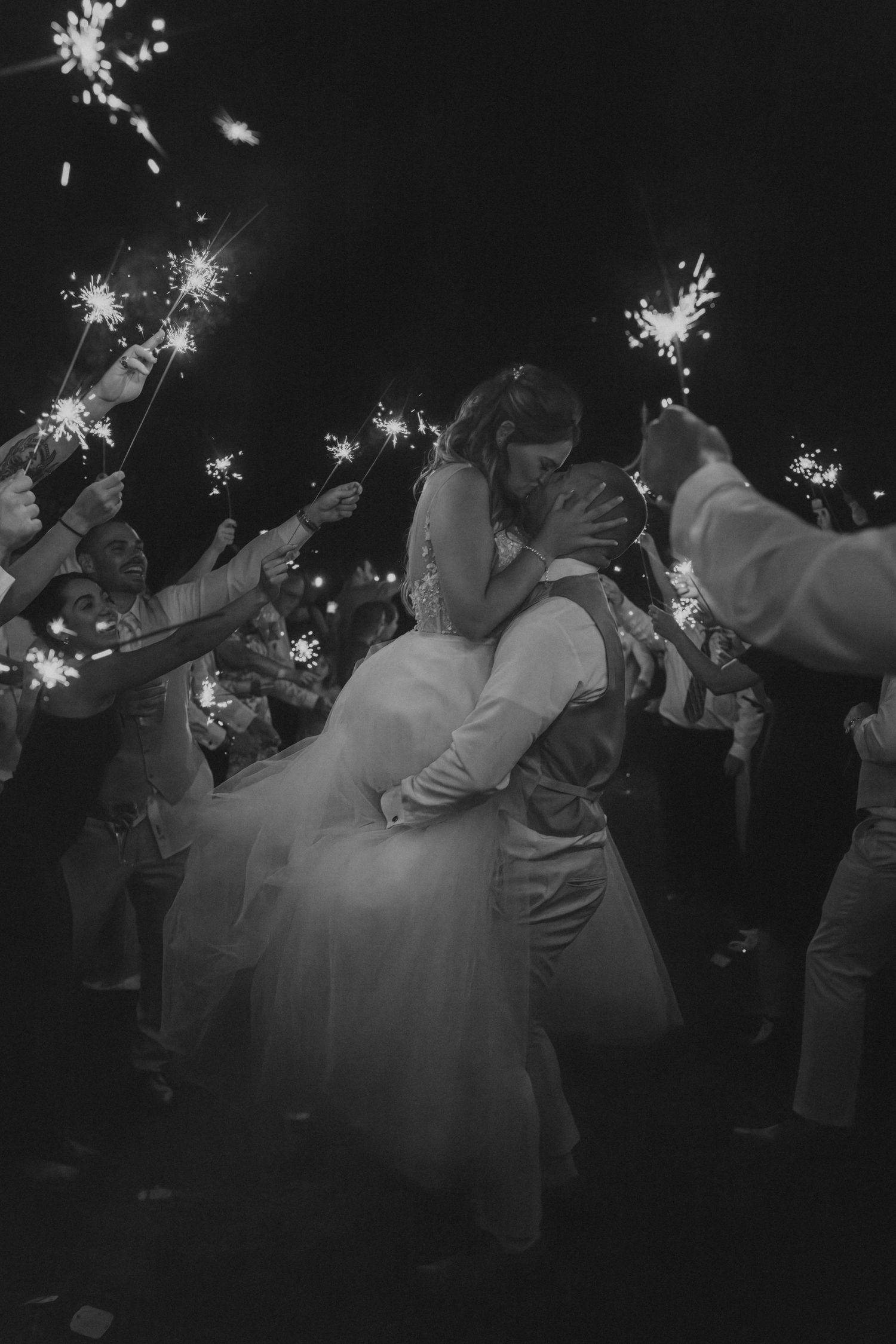 Black and white photo of groom lifting bride during romantic sparkler exit at wedding.