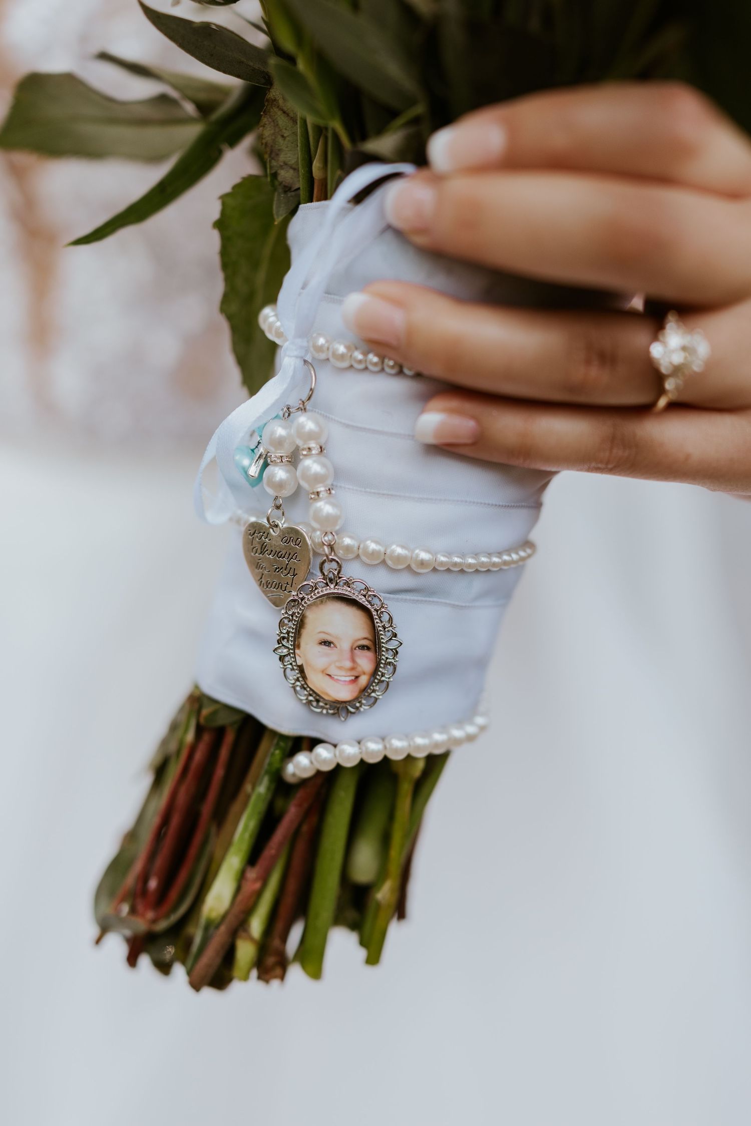 Bridal bouquet adorned with pearl bracelet and photo memorial charm wrapped in blue ribbon.