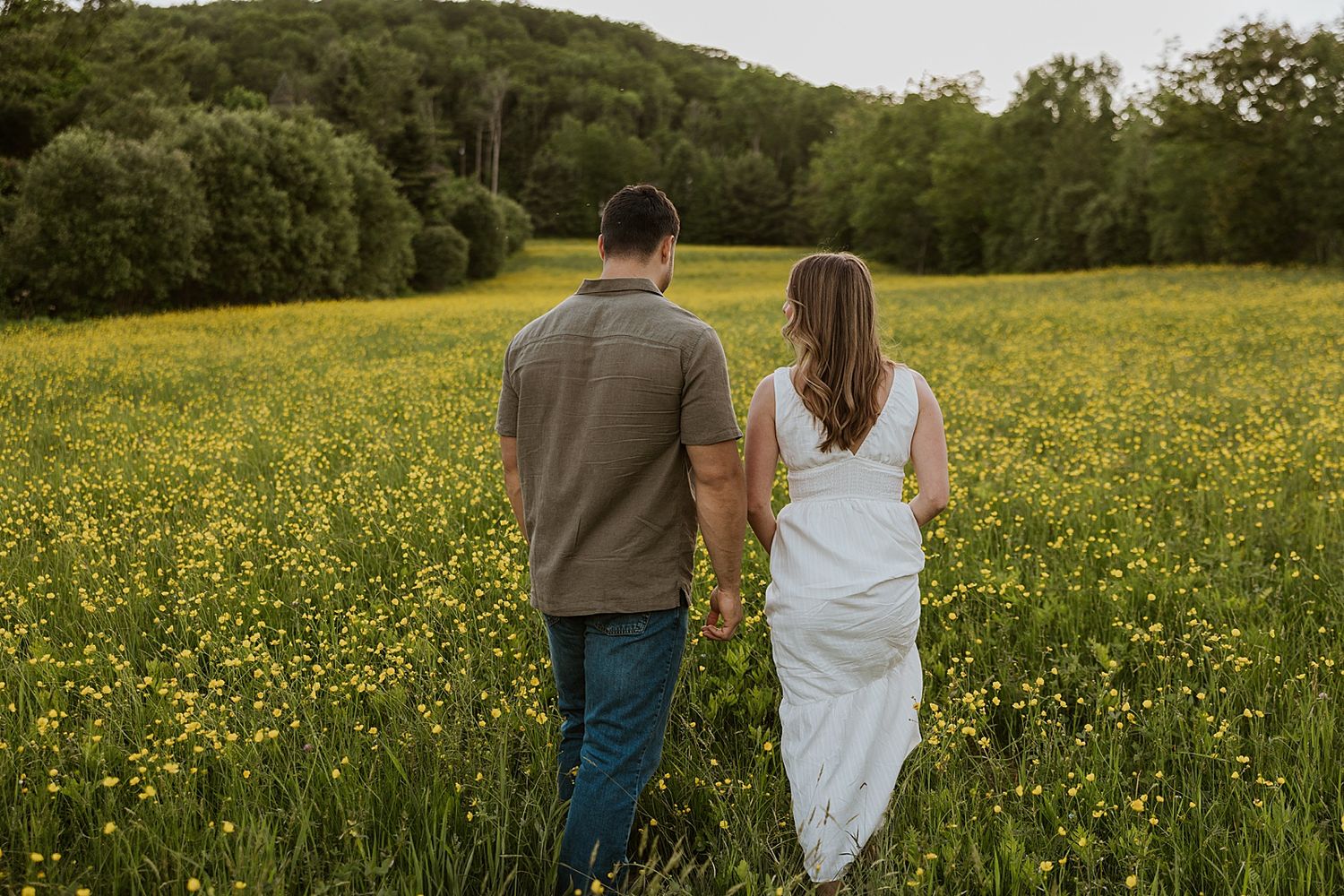 Couple walking through a wildflower field taking golden hour engagement photos in New Hampshire