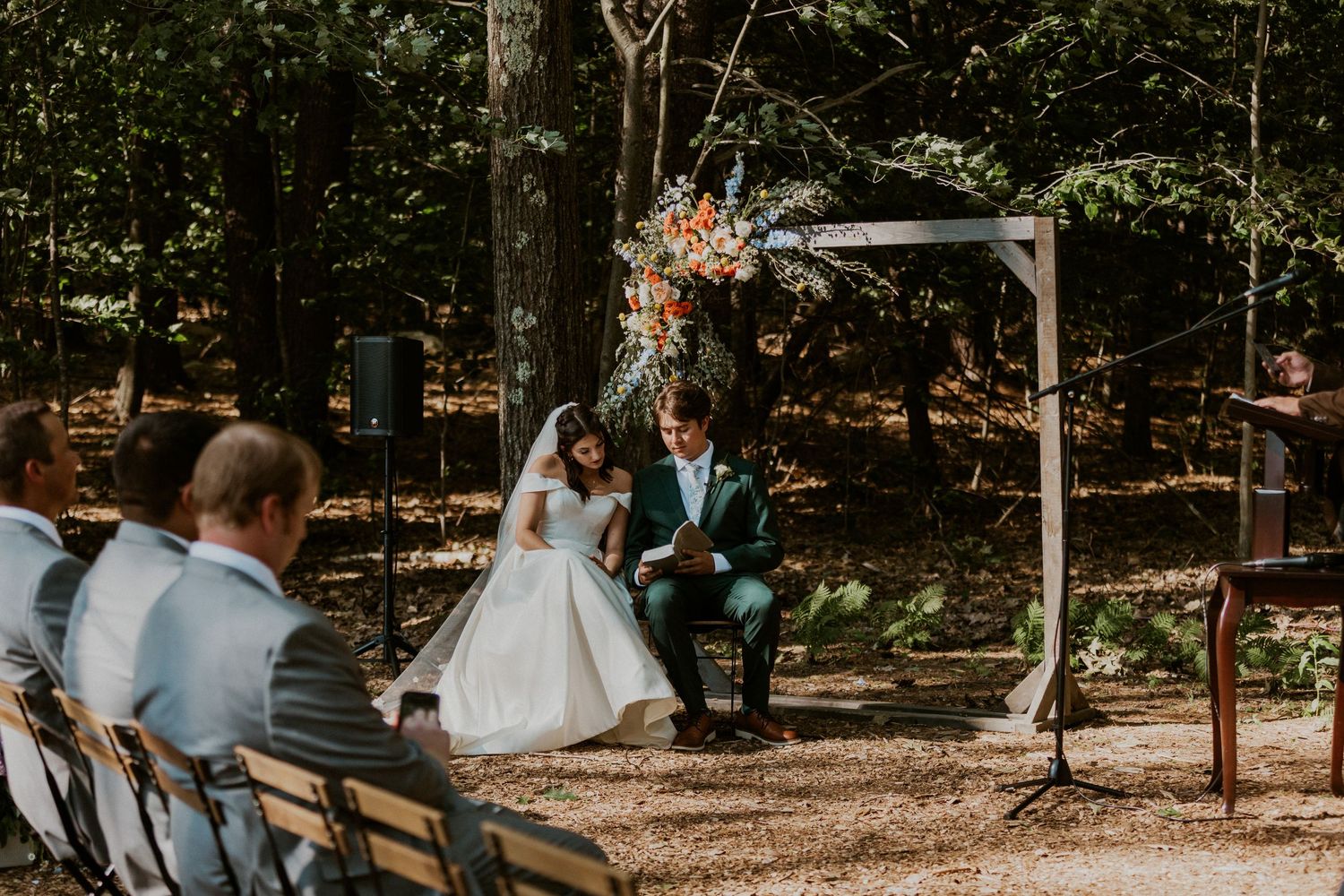 Wedding ceremony setup in a forest with wooden benches and floral decorations.