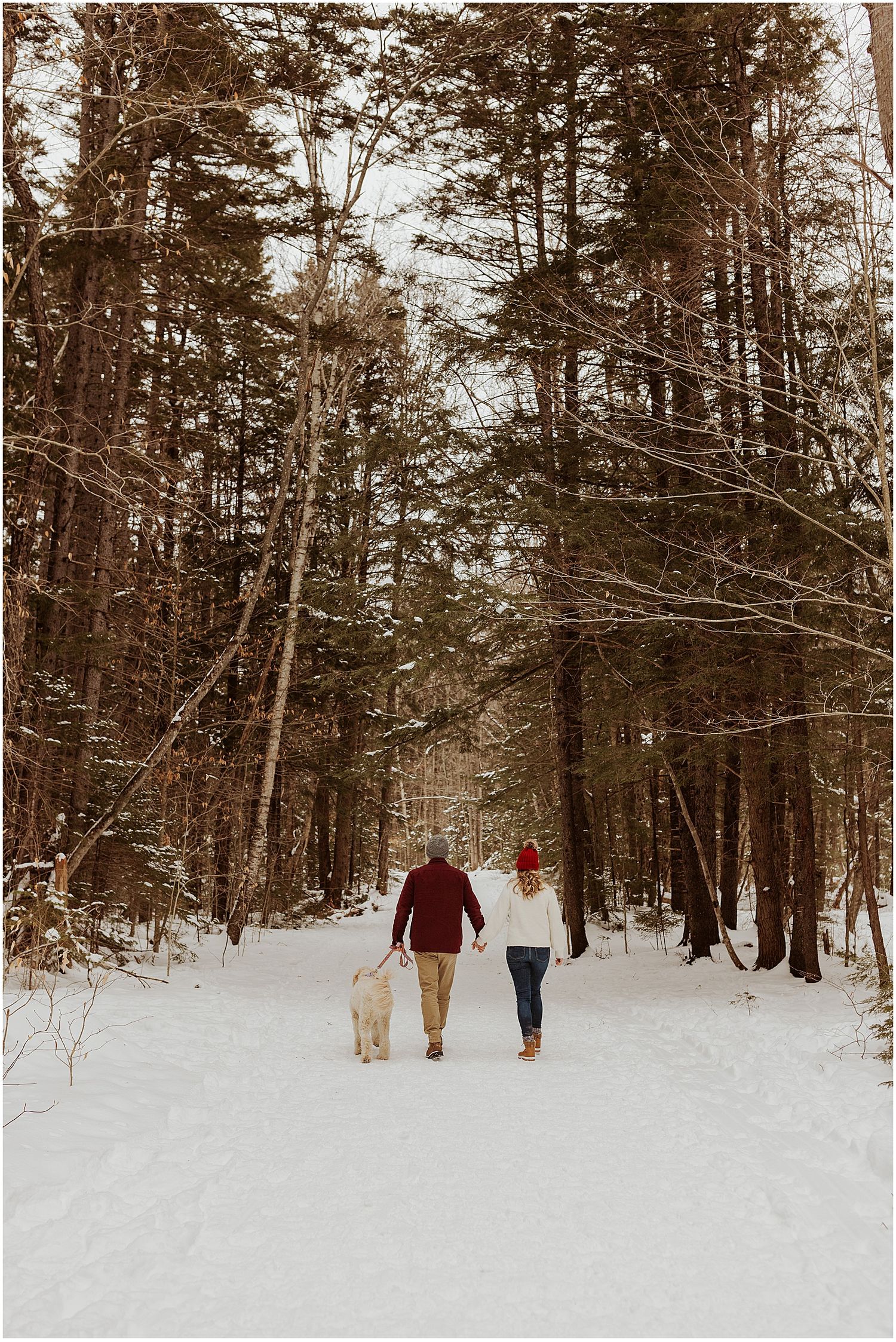 Walking through a snowy forest path during winter engagement photo session.