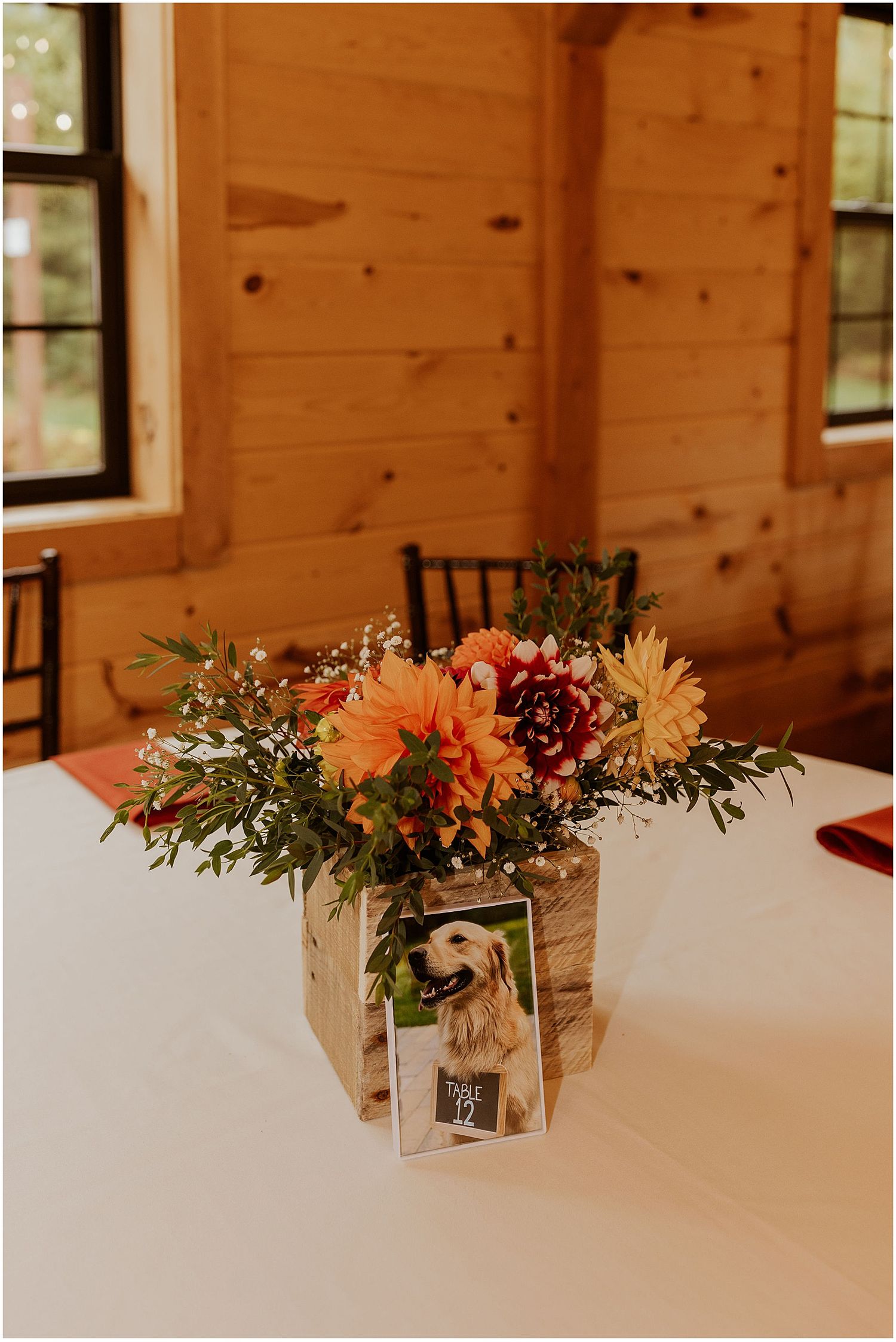 Elegant floral centerpieces with coral dahlias on white tablecloths in rustic venue.