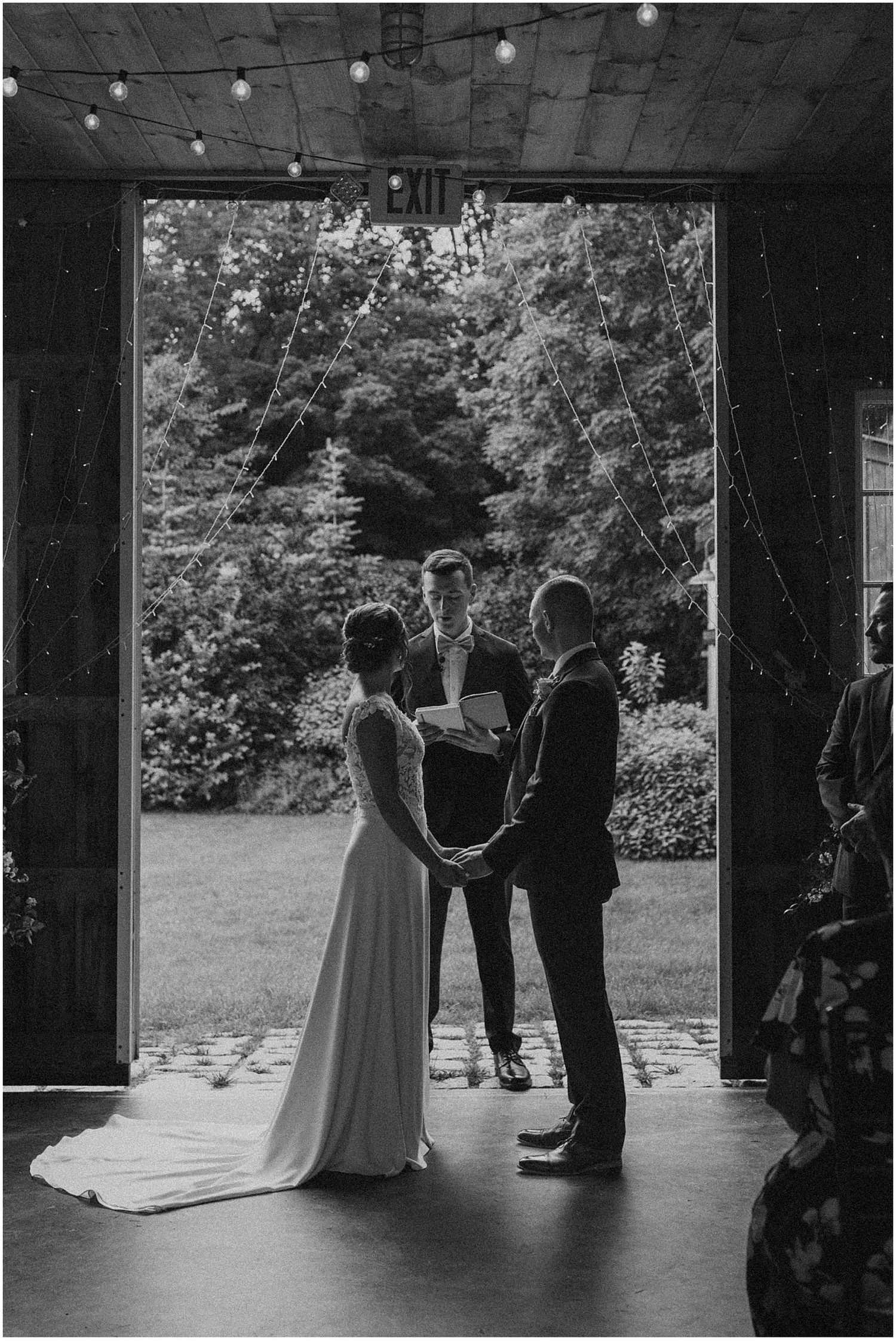 Wedding ceremony silhouettes in a barn doorway with natural light streaming in.