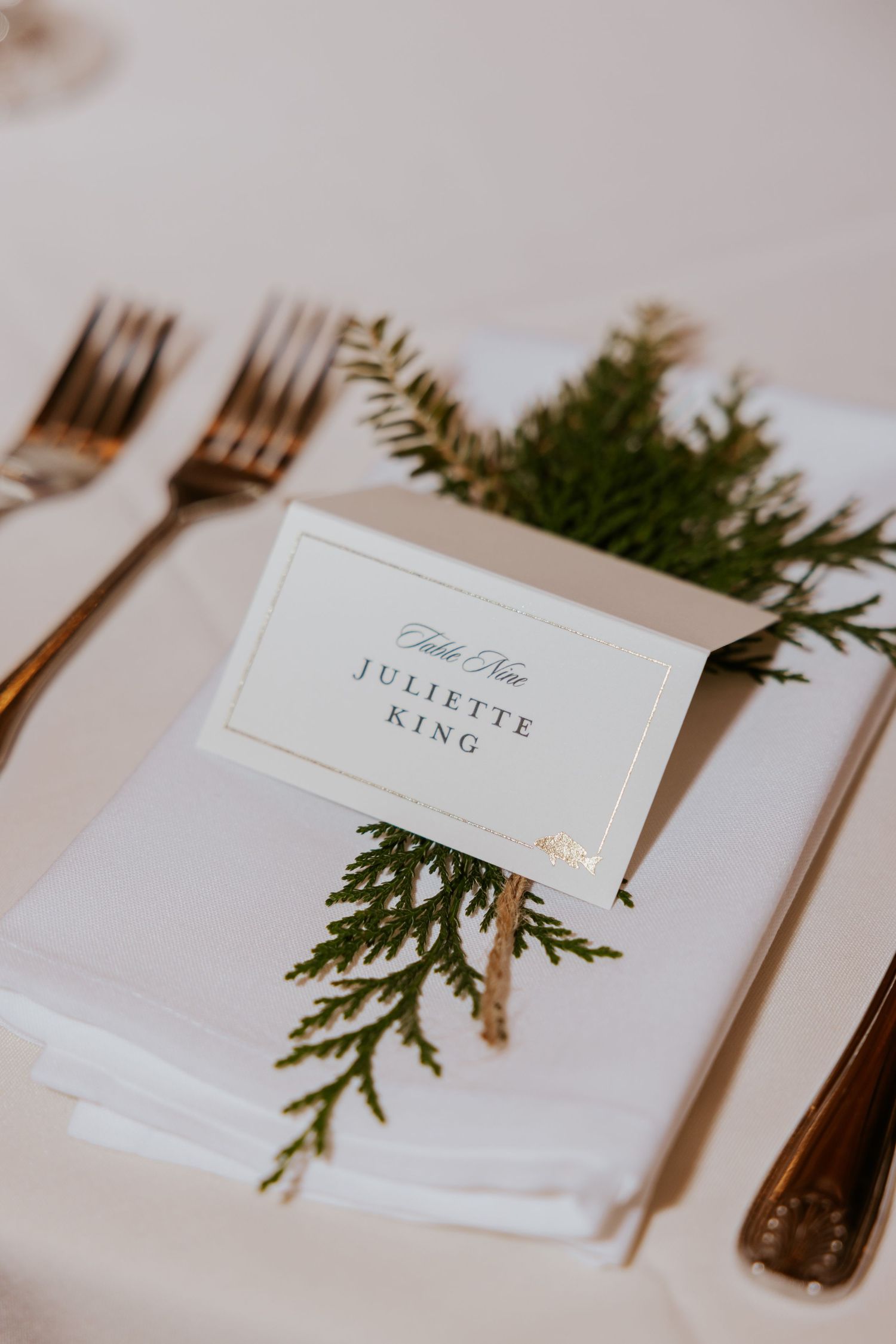 White place cards with evergreen sprigs set on an elegant wedding reception table.