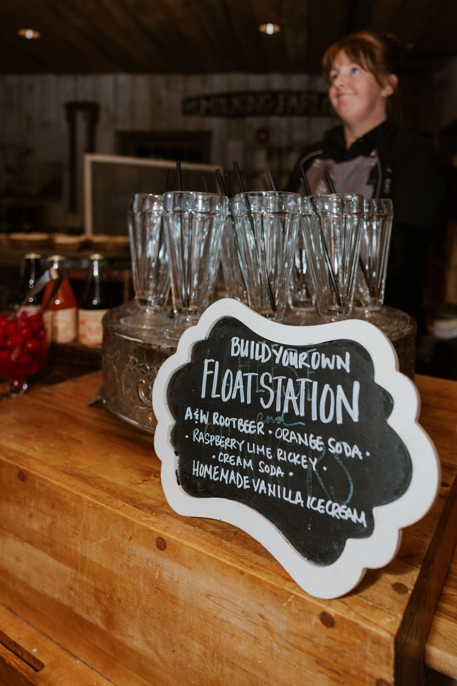 Dessert station with chalkboard signs and empty glasses set up on wooden table at wedding reception.