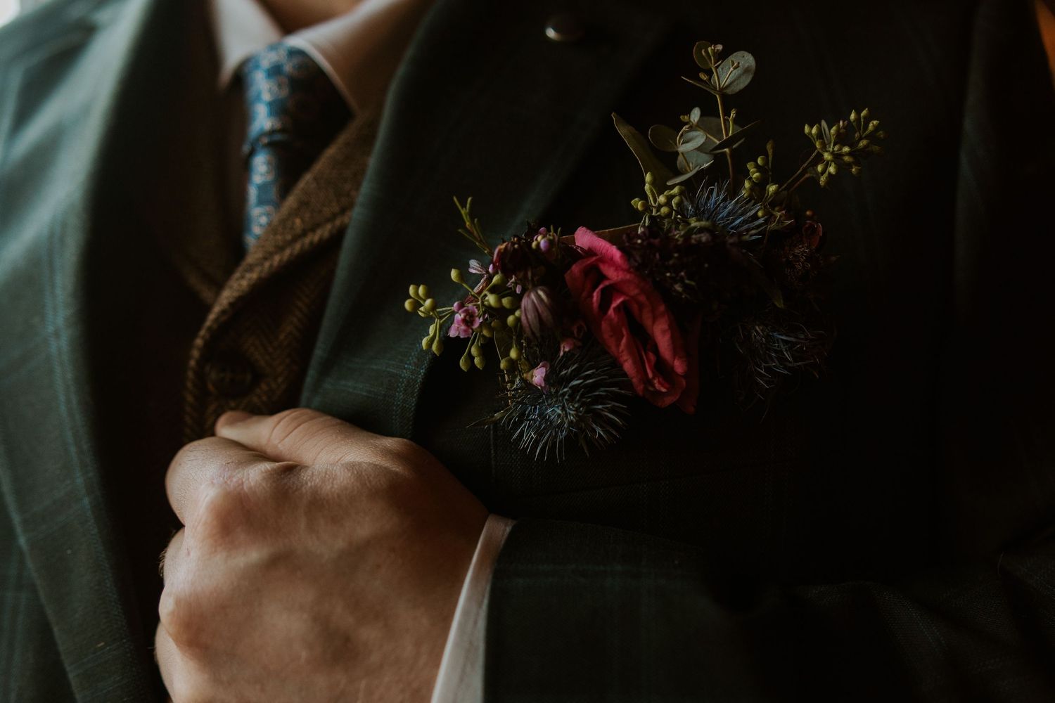 Close-up detail of wedding attire with delicate floral accents in dark moody lighting.