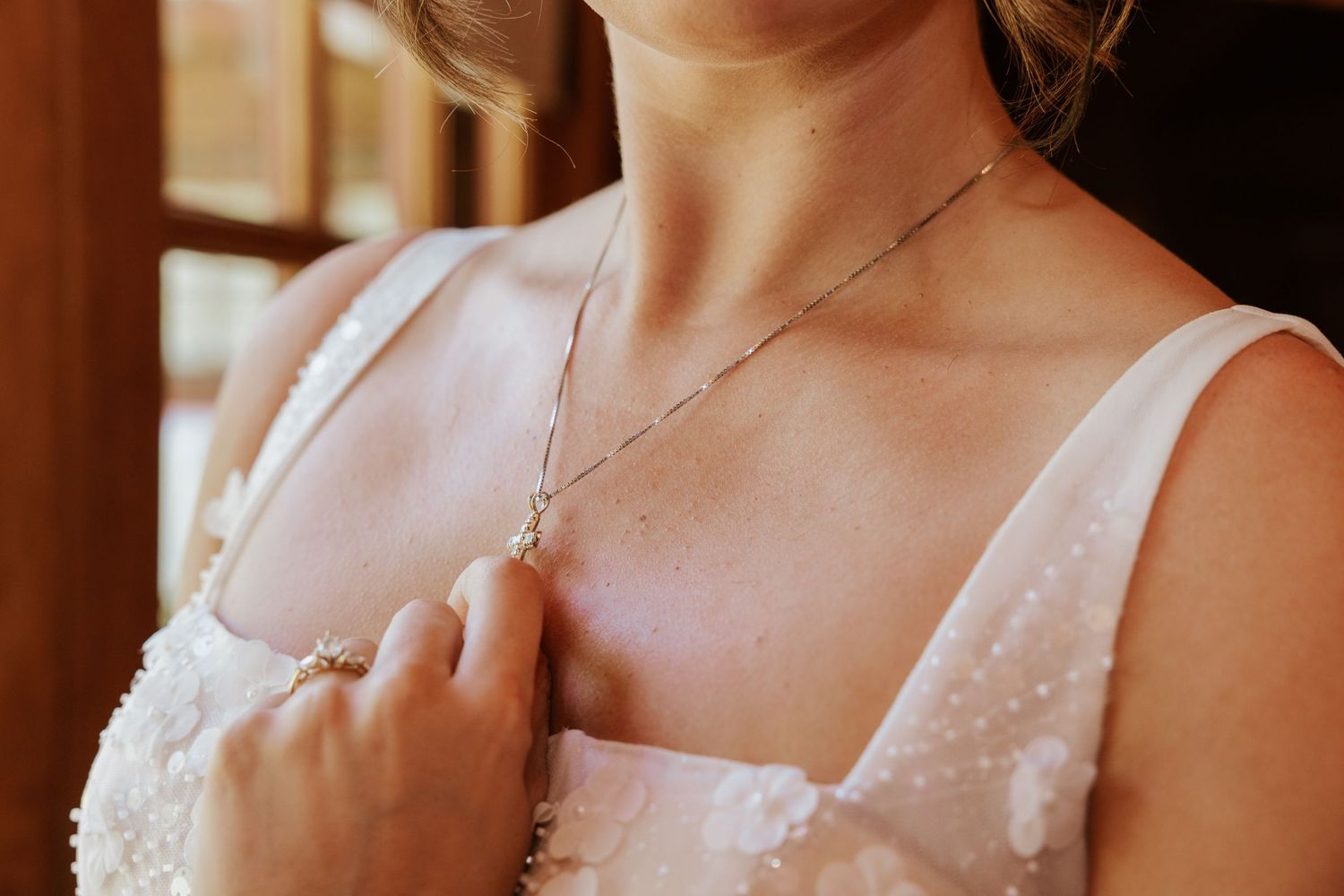 Bride in white dress adjusting pearl necklace with ring on finger, elegant bridal jewelry close-up.