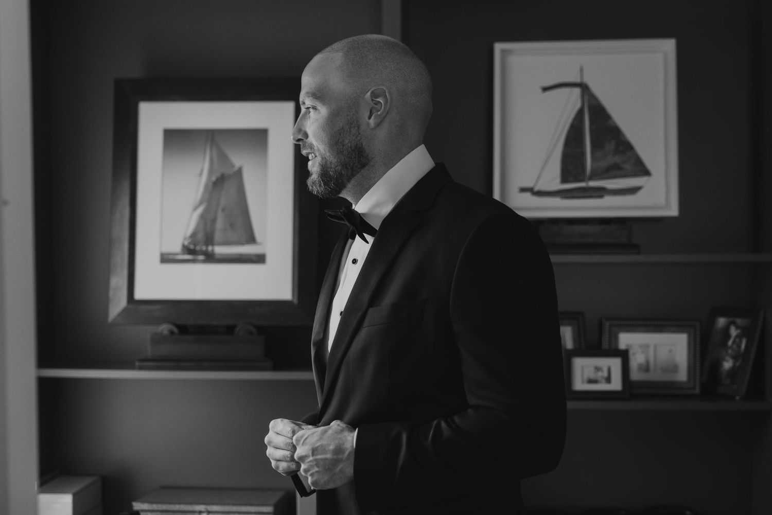 A black and white wedding photo showing a couple sharing a private moment in an elegant room with framed artwork.
