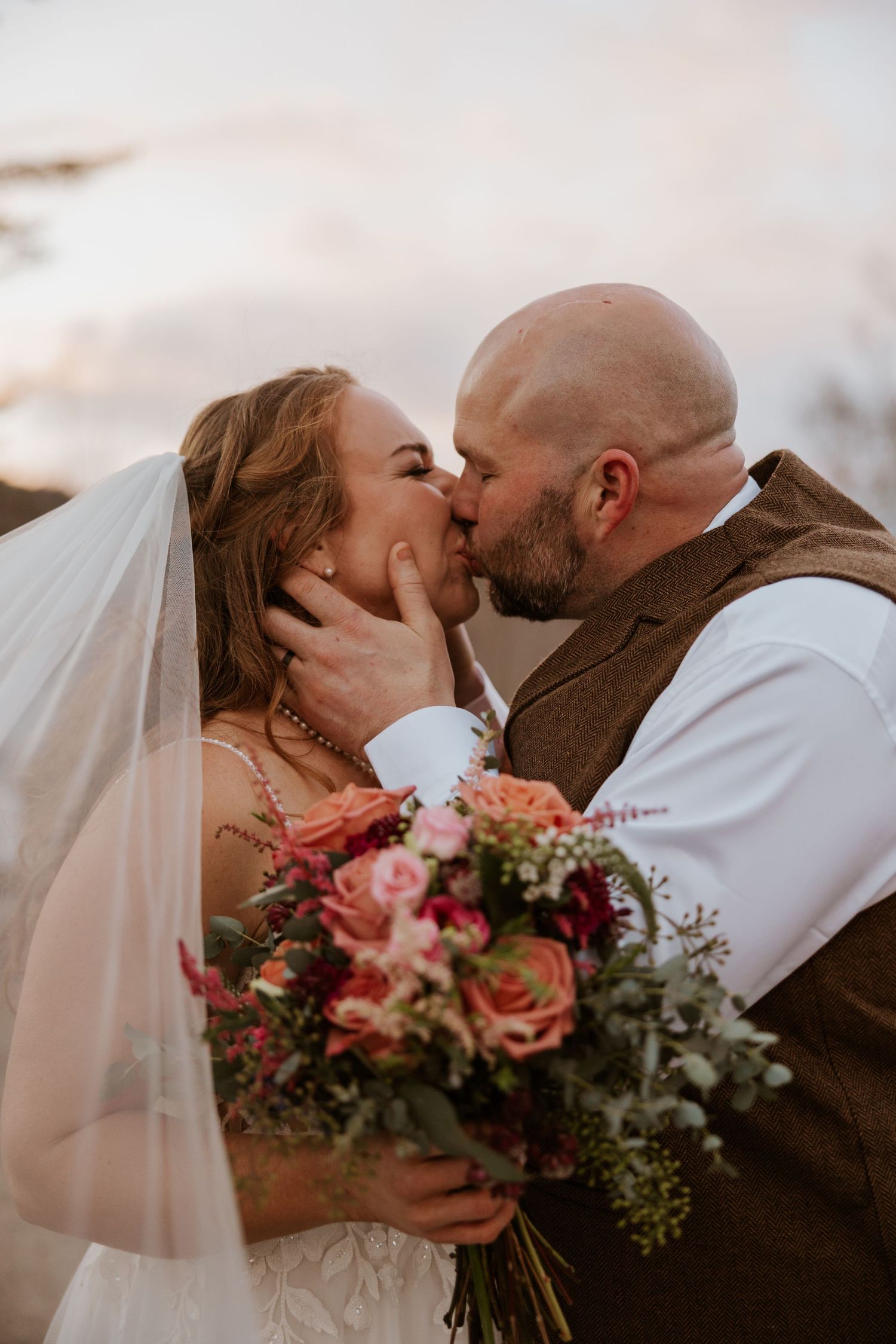 A tender wedding moment at sunset with a colorful bouquet of pink and coral flowers.