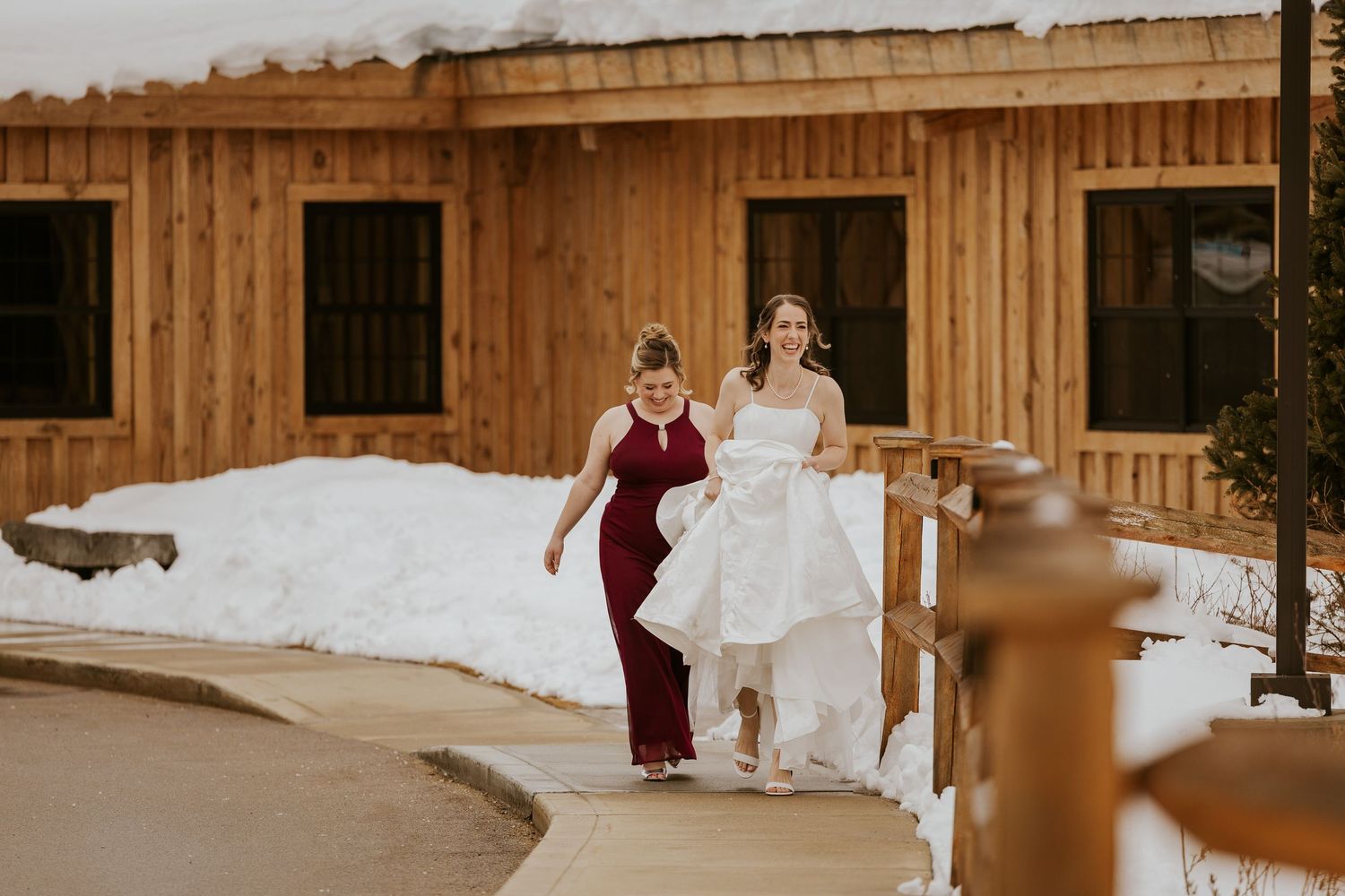 A winter wedding scene with snow on the ground and a rustic wooden barn venue in the background.