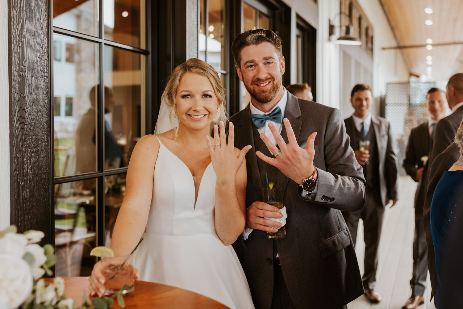 Newlyweds smiling and showing off wedding rings at reception venue after ceremony.