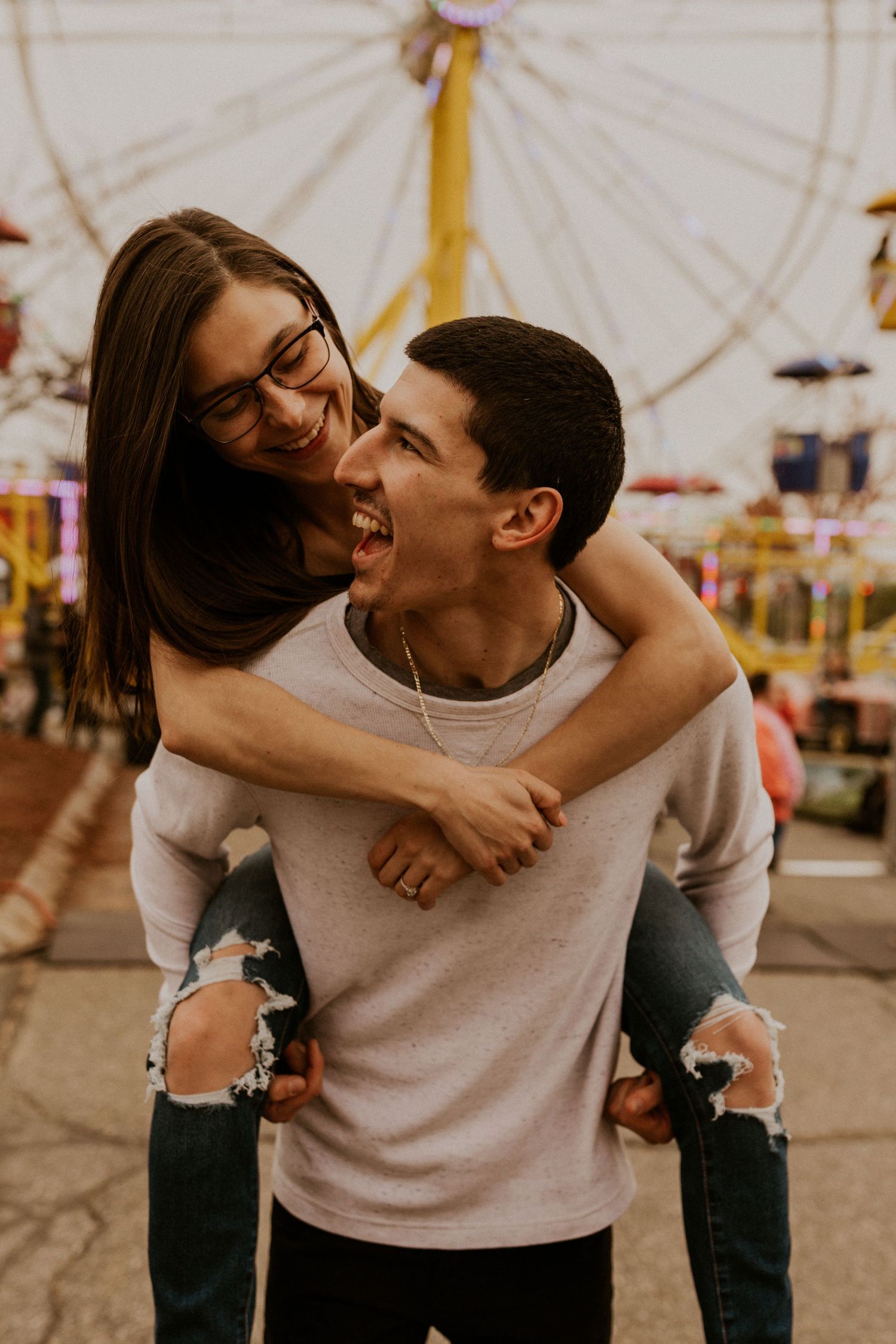 Affectionate couple laughing together at a carnival with a ferris wheel backdrop.