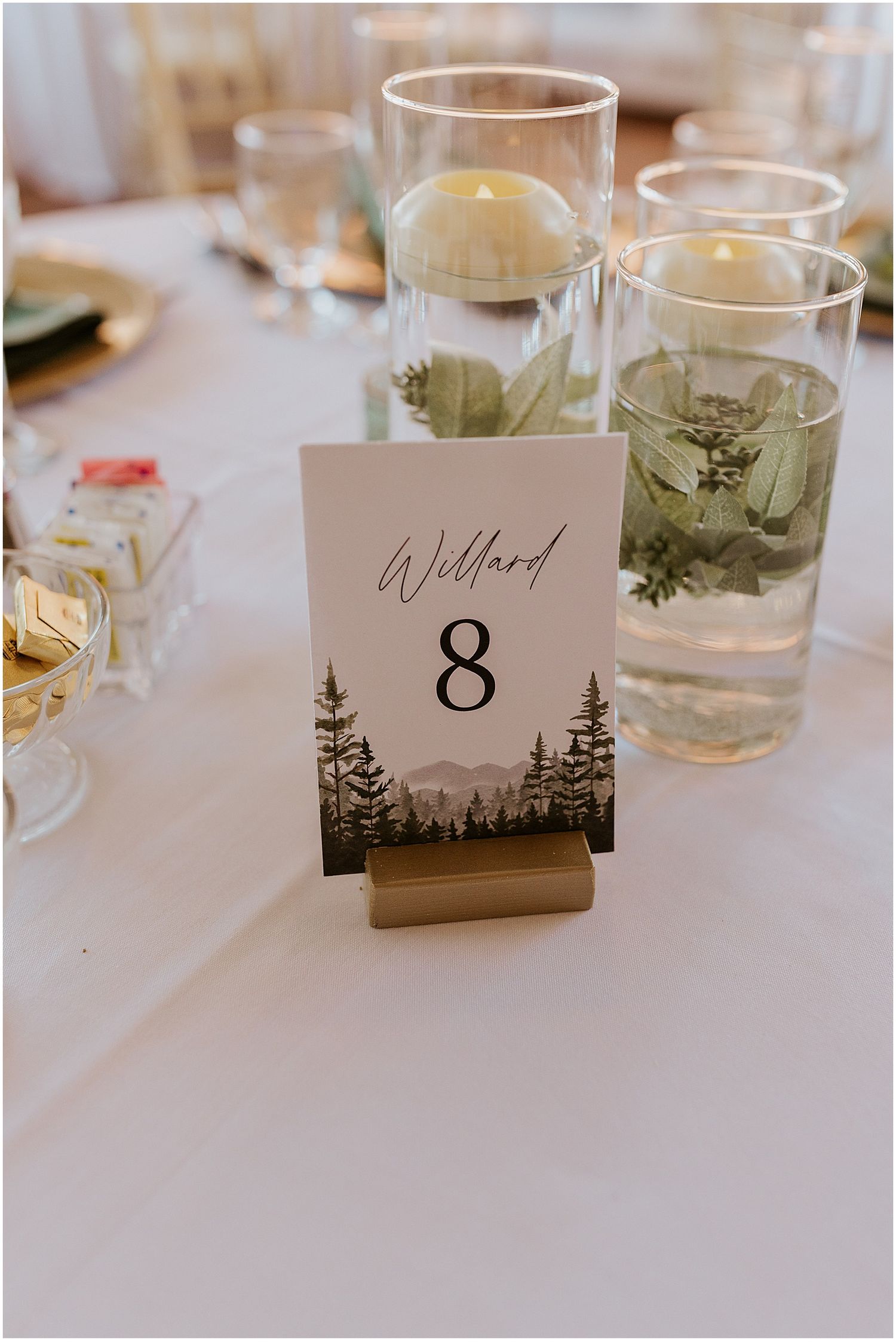 Rustic woodland-themed table number card with pine tree silhouettes in gold stand.