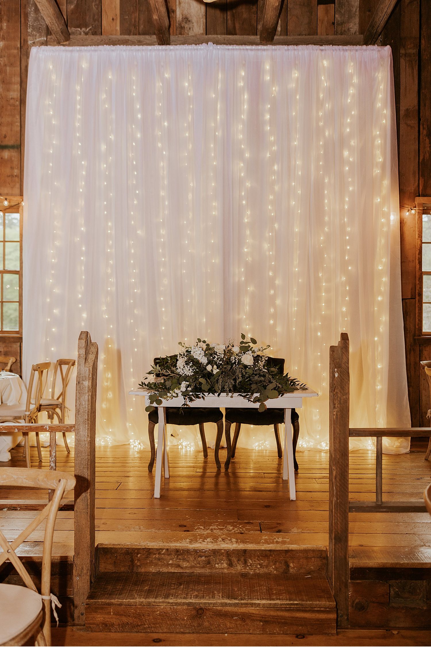 Rustic barn reception setup with fairy light backdrop and wooden details.