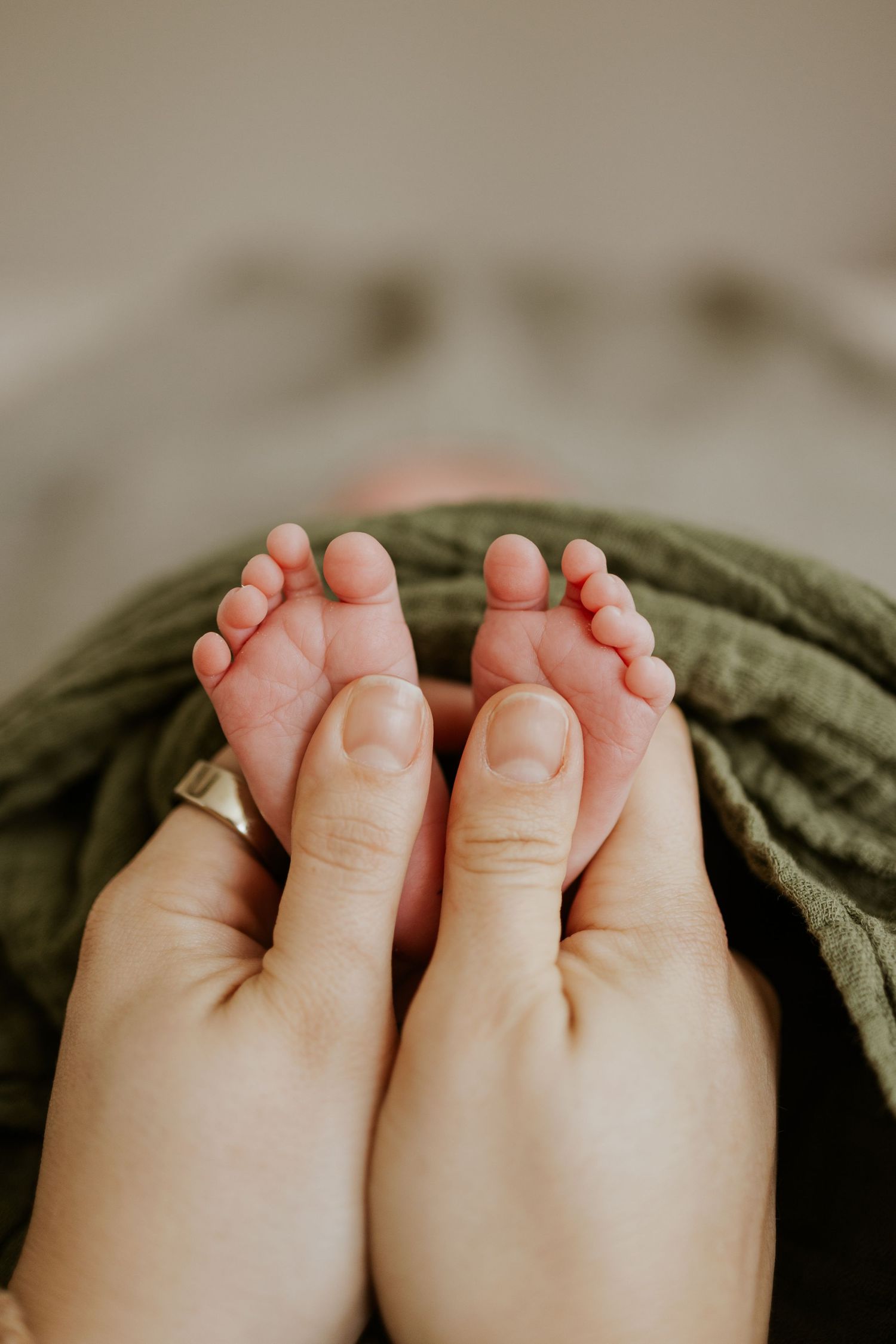 Close-up of tiny newborn baby feet held gently by parent hands wrapped in green swaddle.