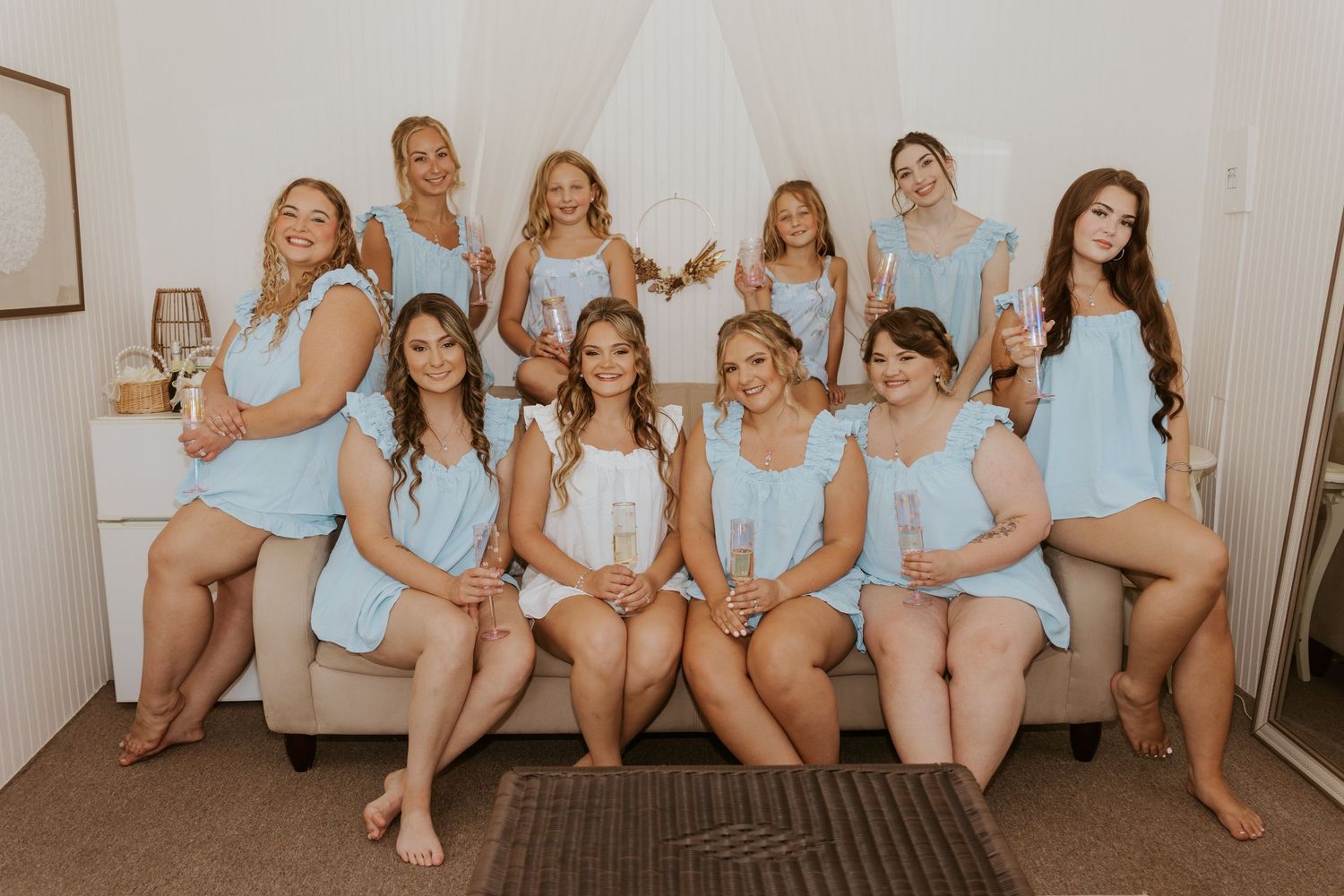 Bridesmaids in matching light blue pajamas posing together on a couch holding champagne glasses.