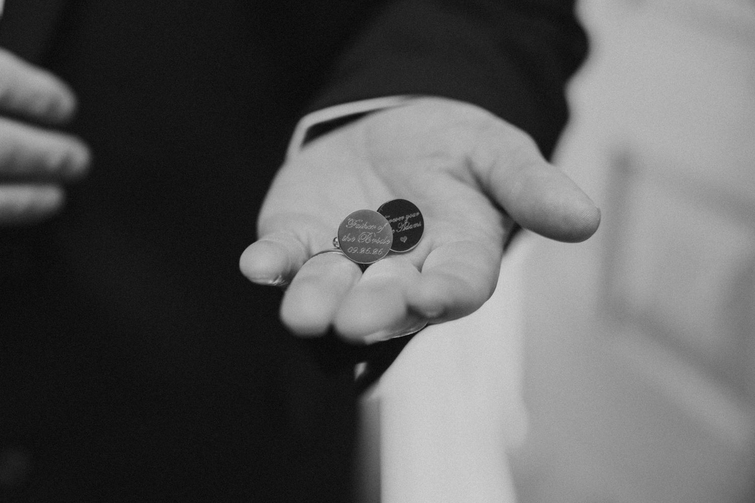 Black and white photo of a groom holding a small heart-shaped keepsake token in his open palm.
