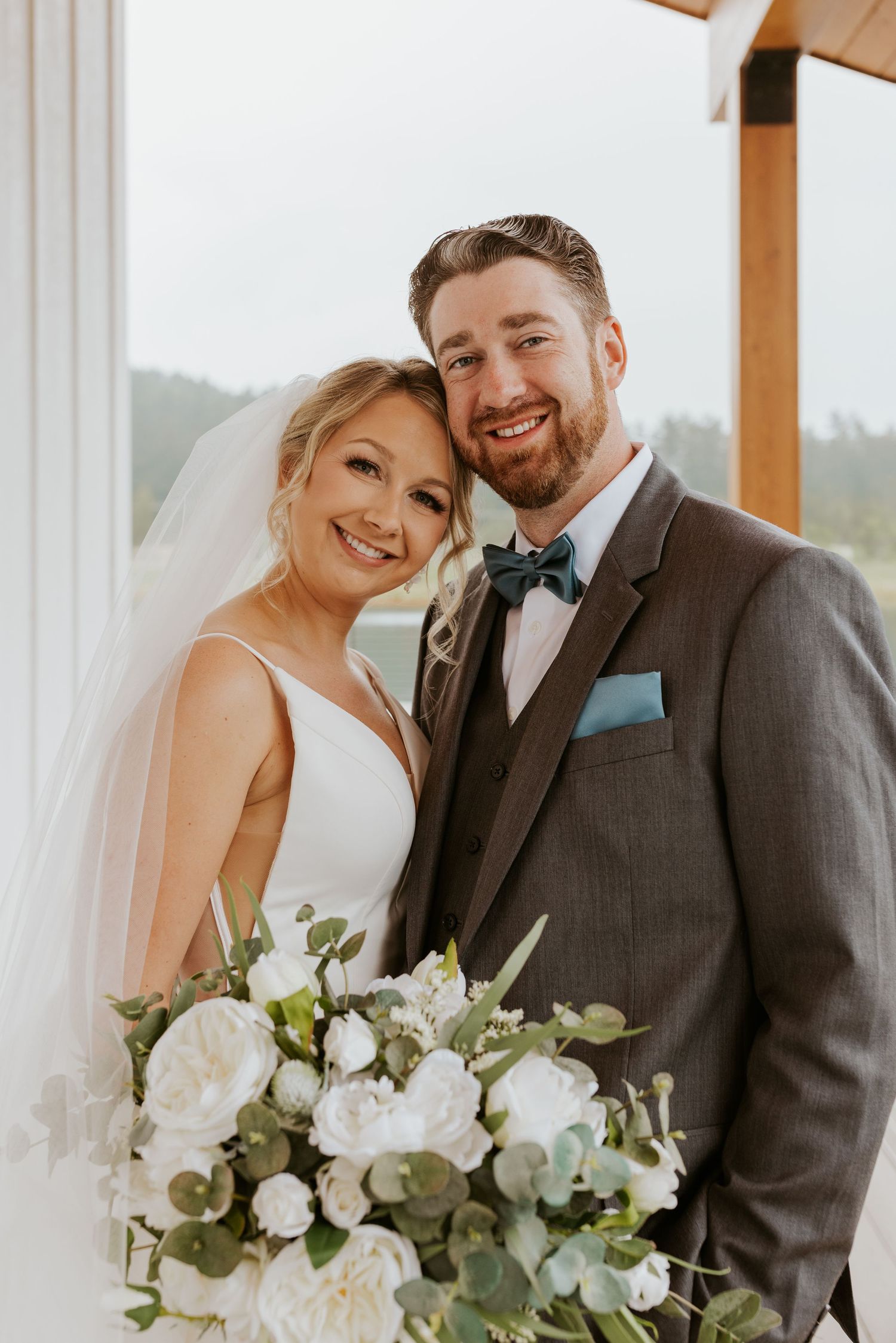 Smiling bride and groom posing together holding a white peony bouquet with eucalyptus greenery.