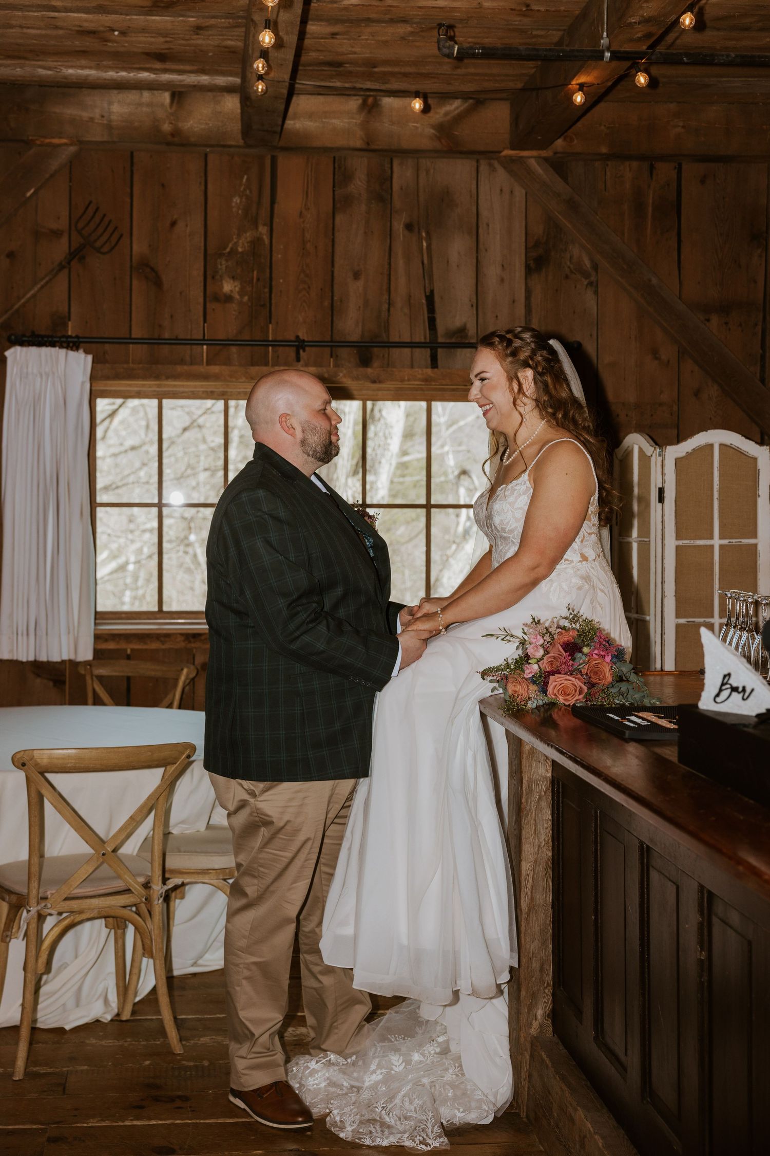 Intimate wedding ceremony taking place inside a cozy wooden barn with string lights overhead.