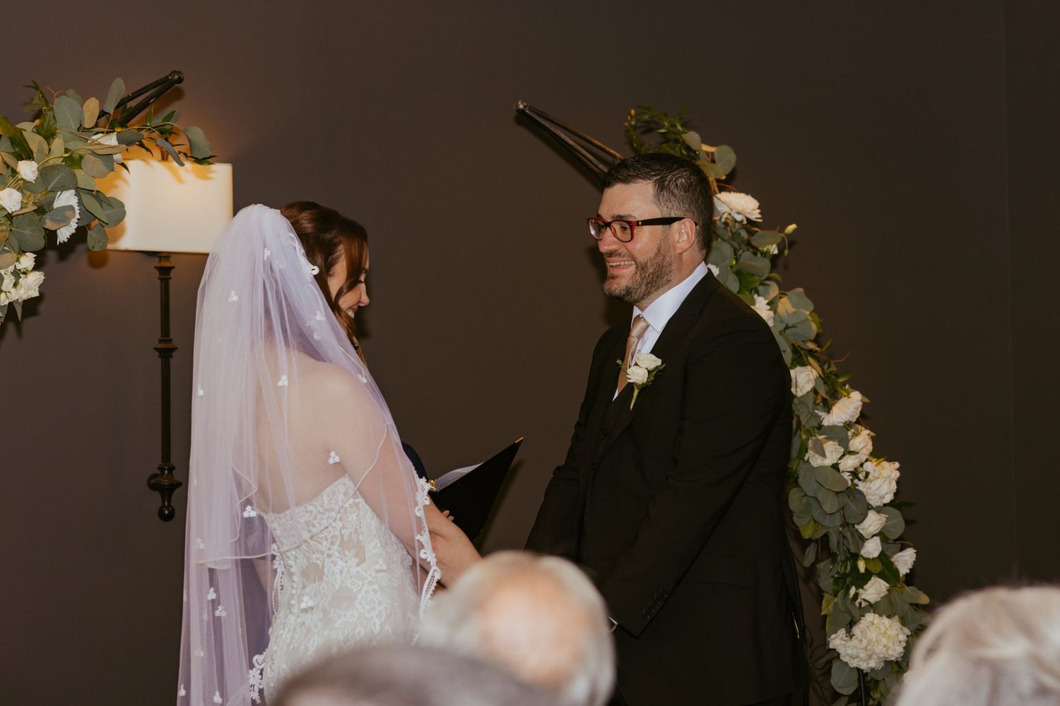 A romantic first look between newlyweds in front of elegant floral arrangements at an indoor venue.