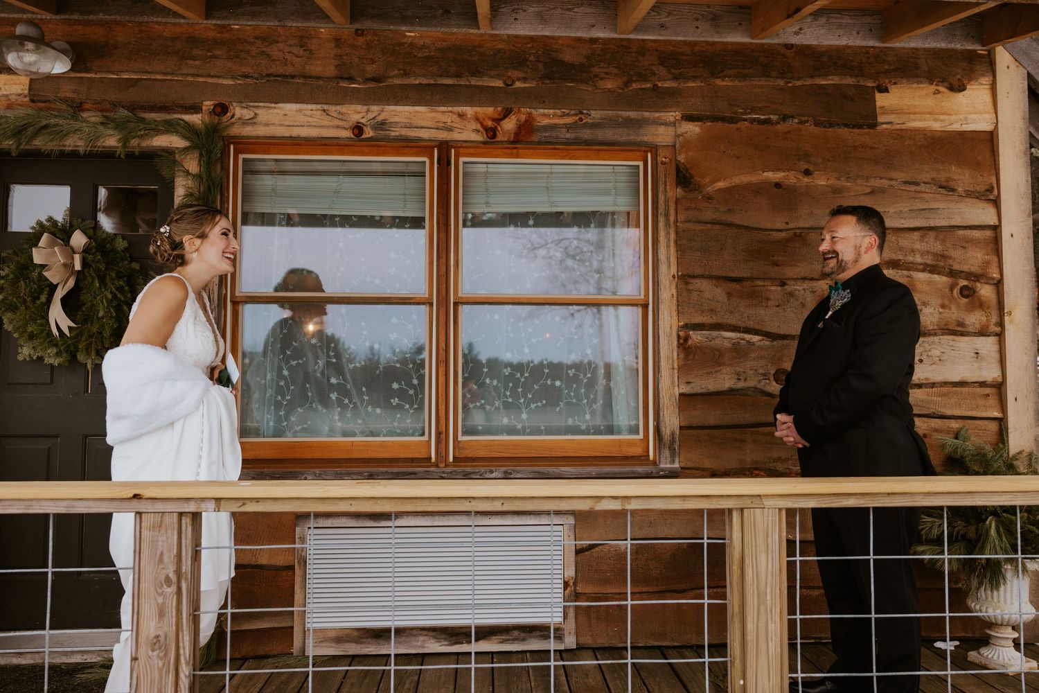 Bride and groom share first look on rustic log cabin porch during outdoor wedding ceremony.