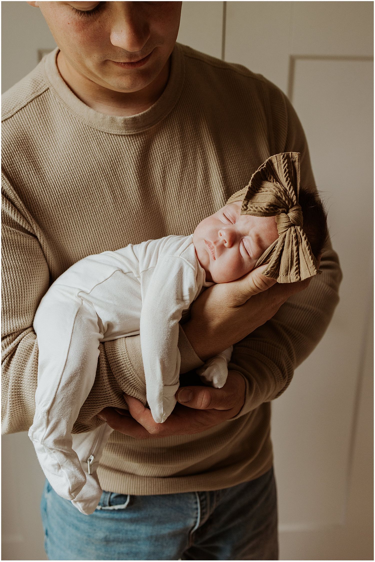 Newborn baby sleeping on her dad's arm while they take lifestyle newborn family photos at home in New Hampshire