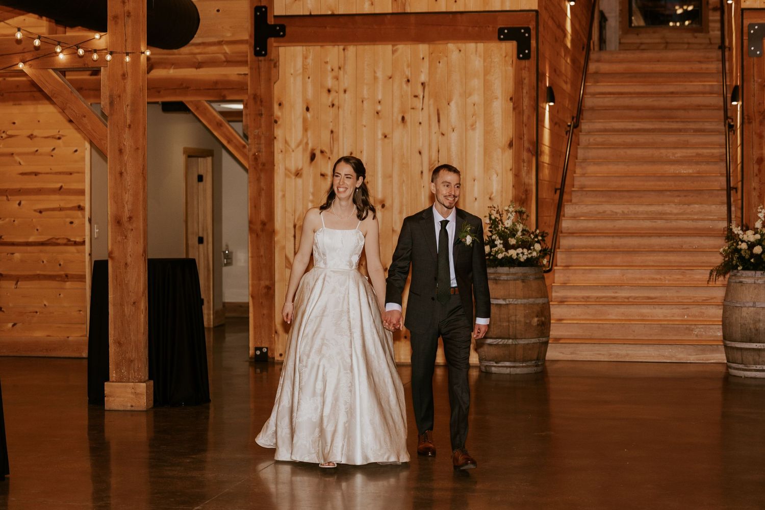 A wedding couple walks together through an elegant wooden-paneled venue with warm lighting and rustic charm.