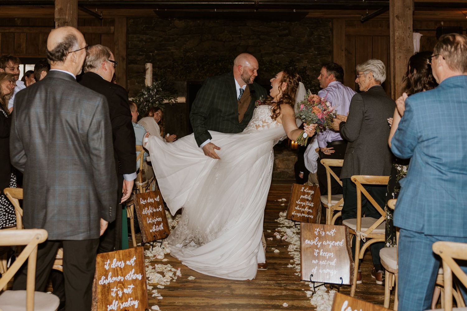 Wedding reception guests dancing and celebrating inside a rustic wooden venue with string lights.