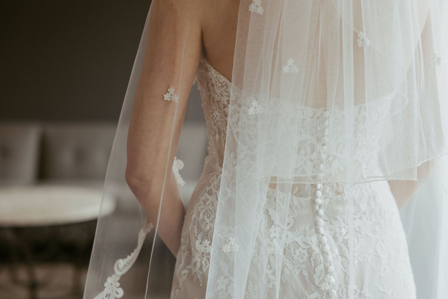 Close-up details of a white lace wedding dress with delicate embroidery and beading against a light background.