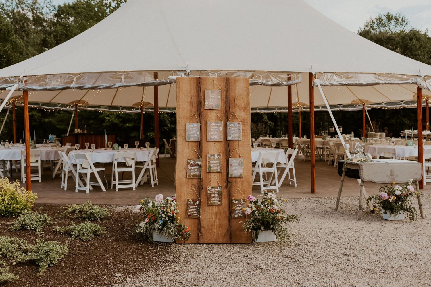 Large white wedding tent setup with wooden posts and folding chairs.