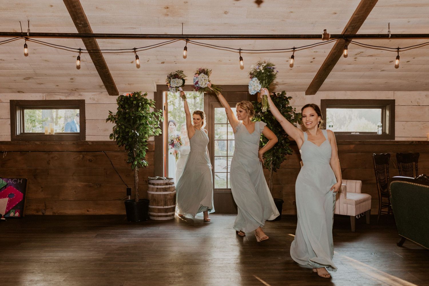 Wedding party dances and celebrates in a wooden barn venue with string lights.