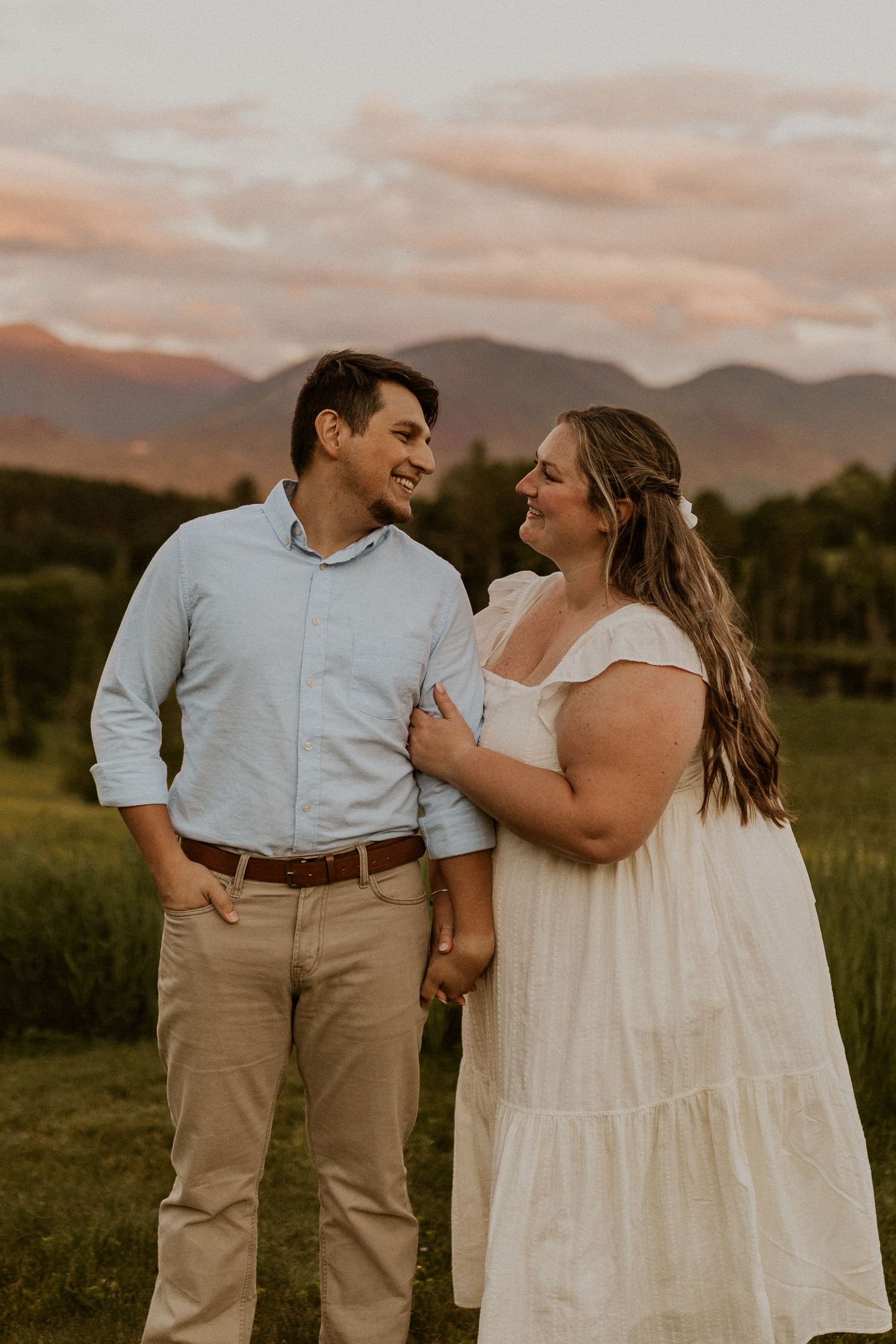 Terise hugging onto Jose's arm and smiling during an engagement photoshoot in the lupine fields of Sugar Hill NH.