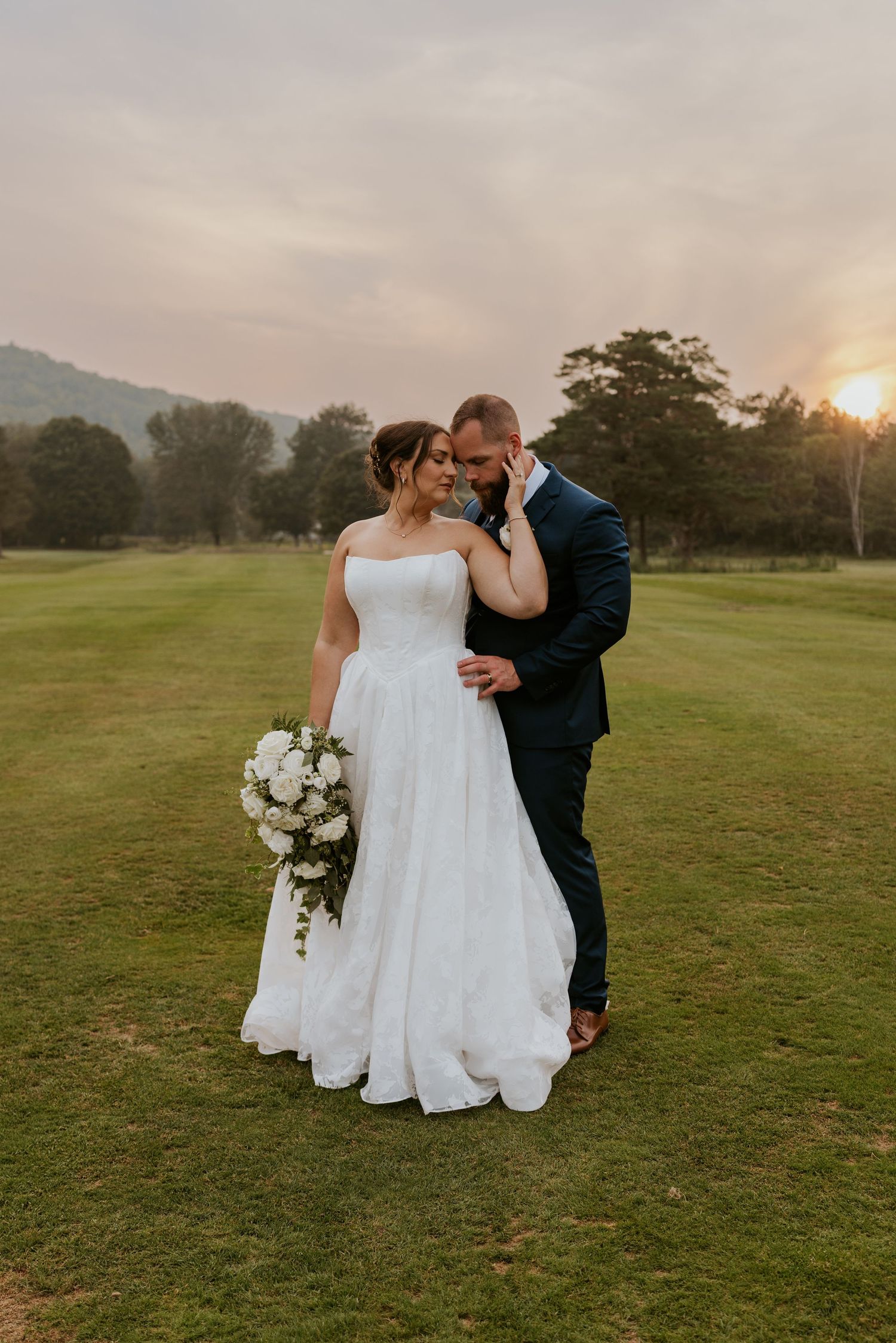 Bride and groom sharing an intimate moment on a lush green golf course during a golden sunset.