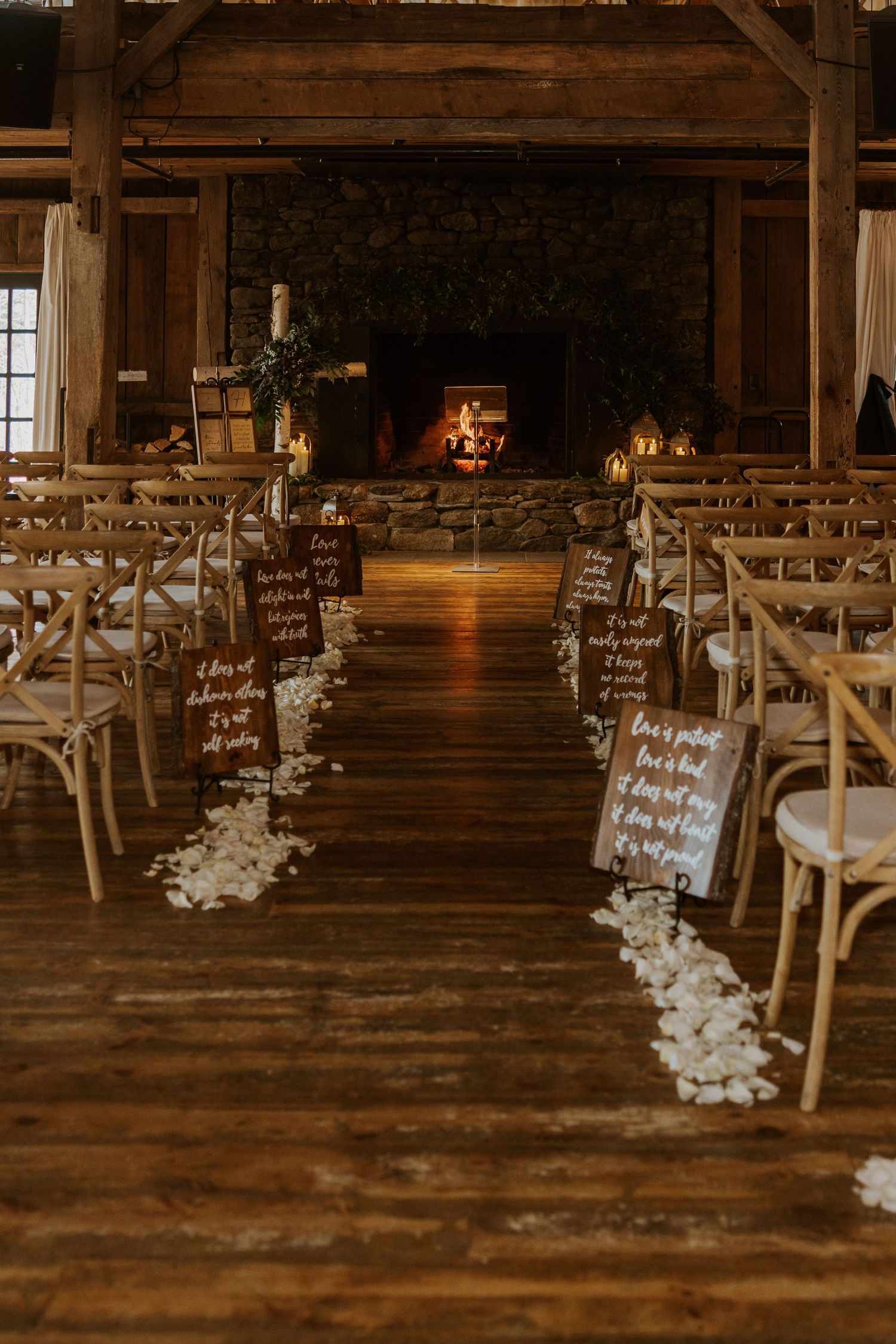 Rustic barn wedding ceremony setup with wooden cross-back chairs and floral aisle decorations on hardwood floors.