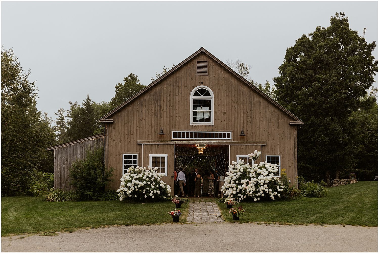 Rustic barn wedding venue exterior decorated with elegant white floral arrangements and natural landscaping.
