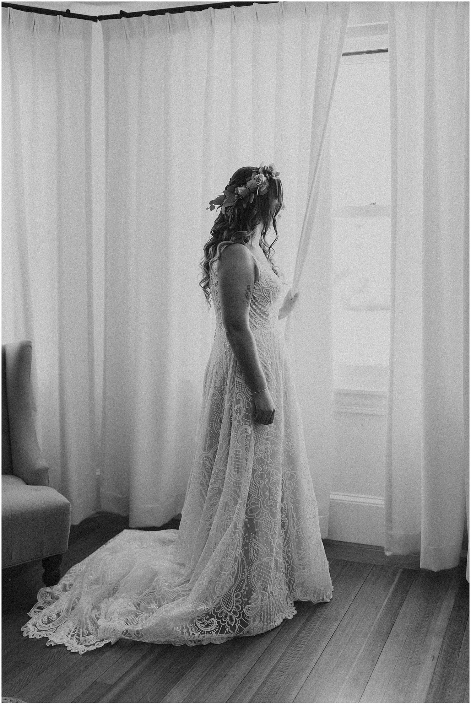 A flowing lace wedding dress with intricate details and train displayed in black and white.