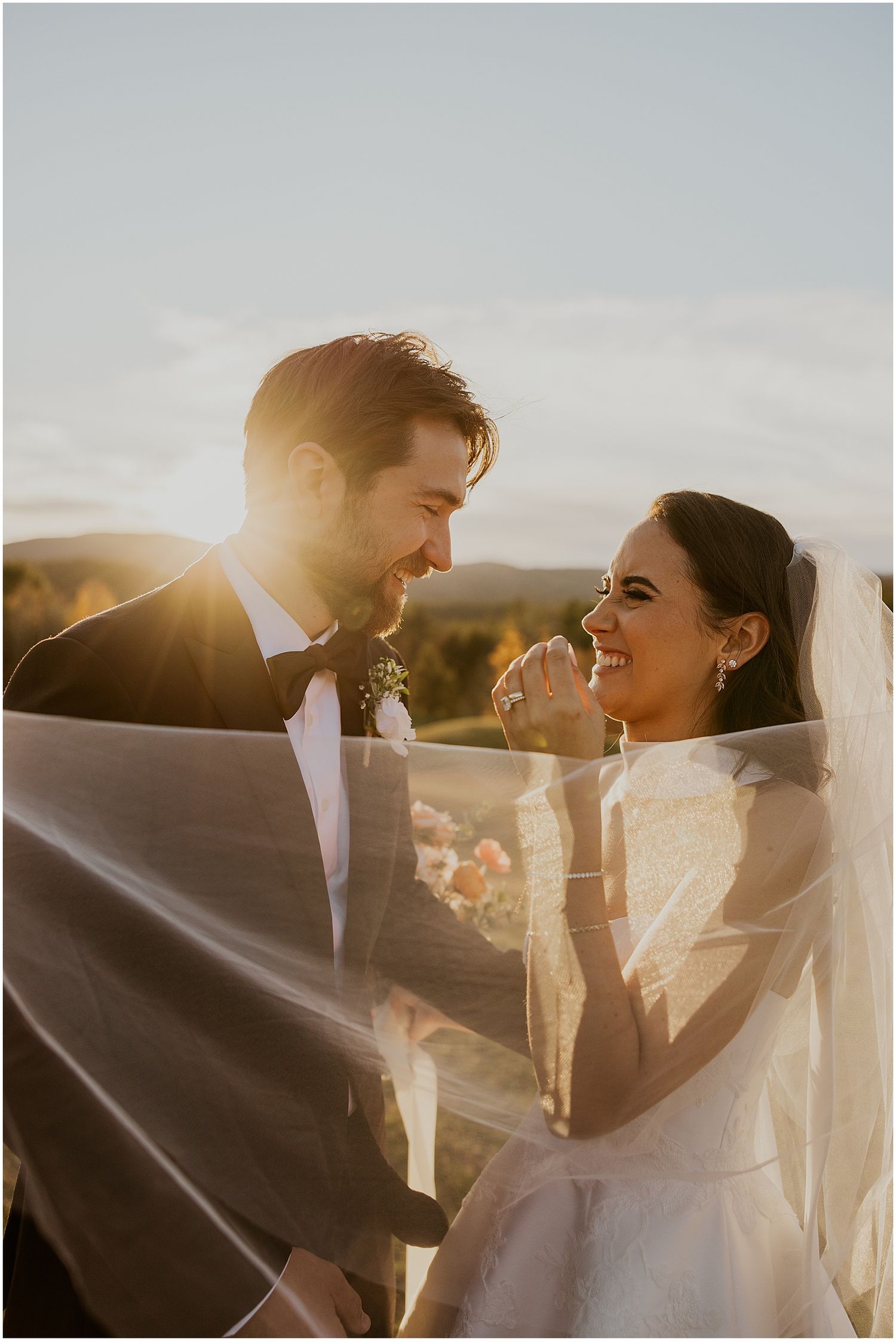 Joyful wedding couple laughing together in warm evening sunlight.