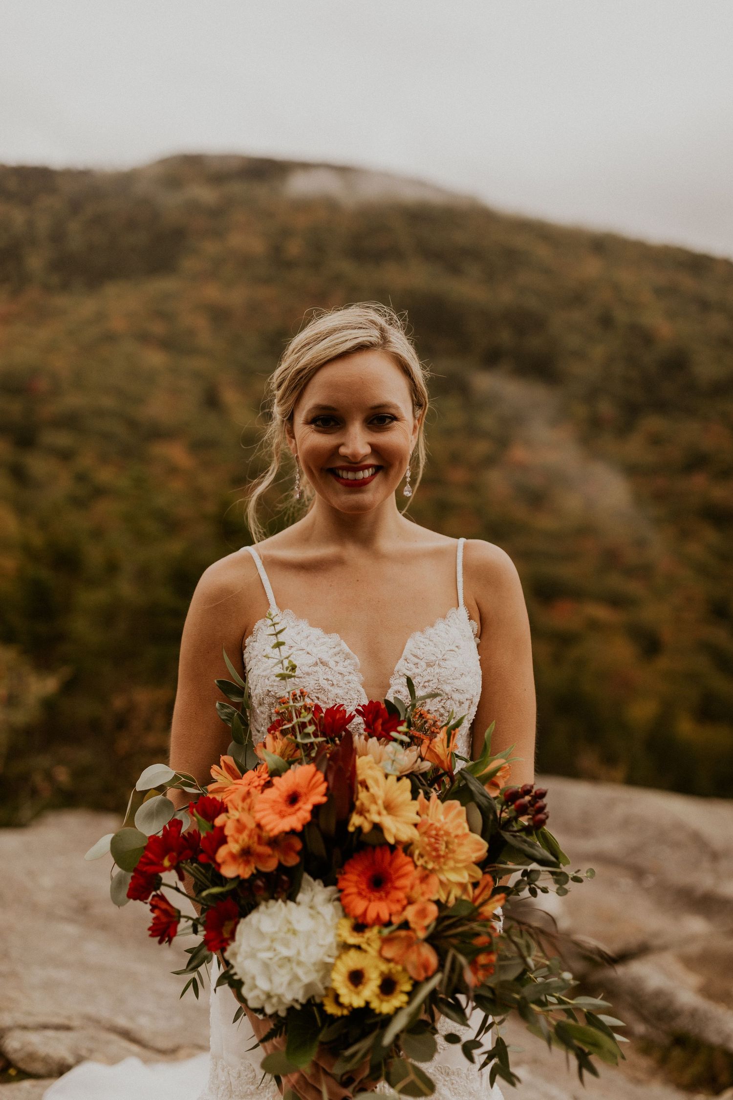 A close up portrait of the bride and her beautiful bouquet filled with yellows, reds and oranges.