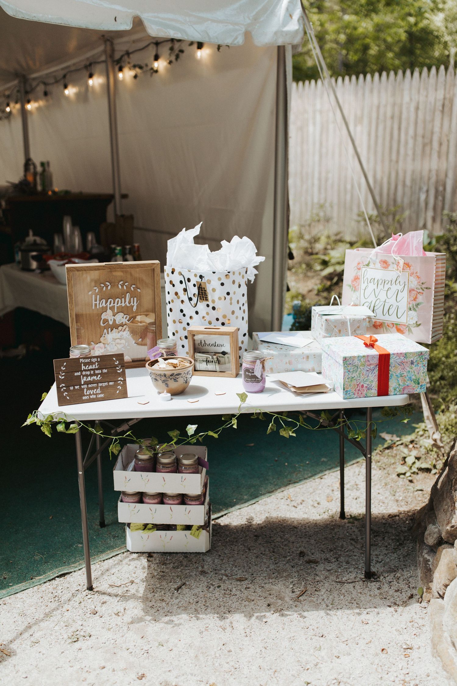 Wedding gift table with rustic decor and string lights under outdoor tent.