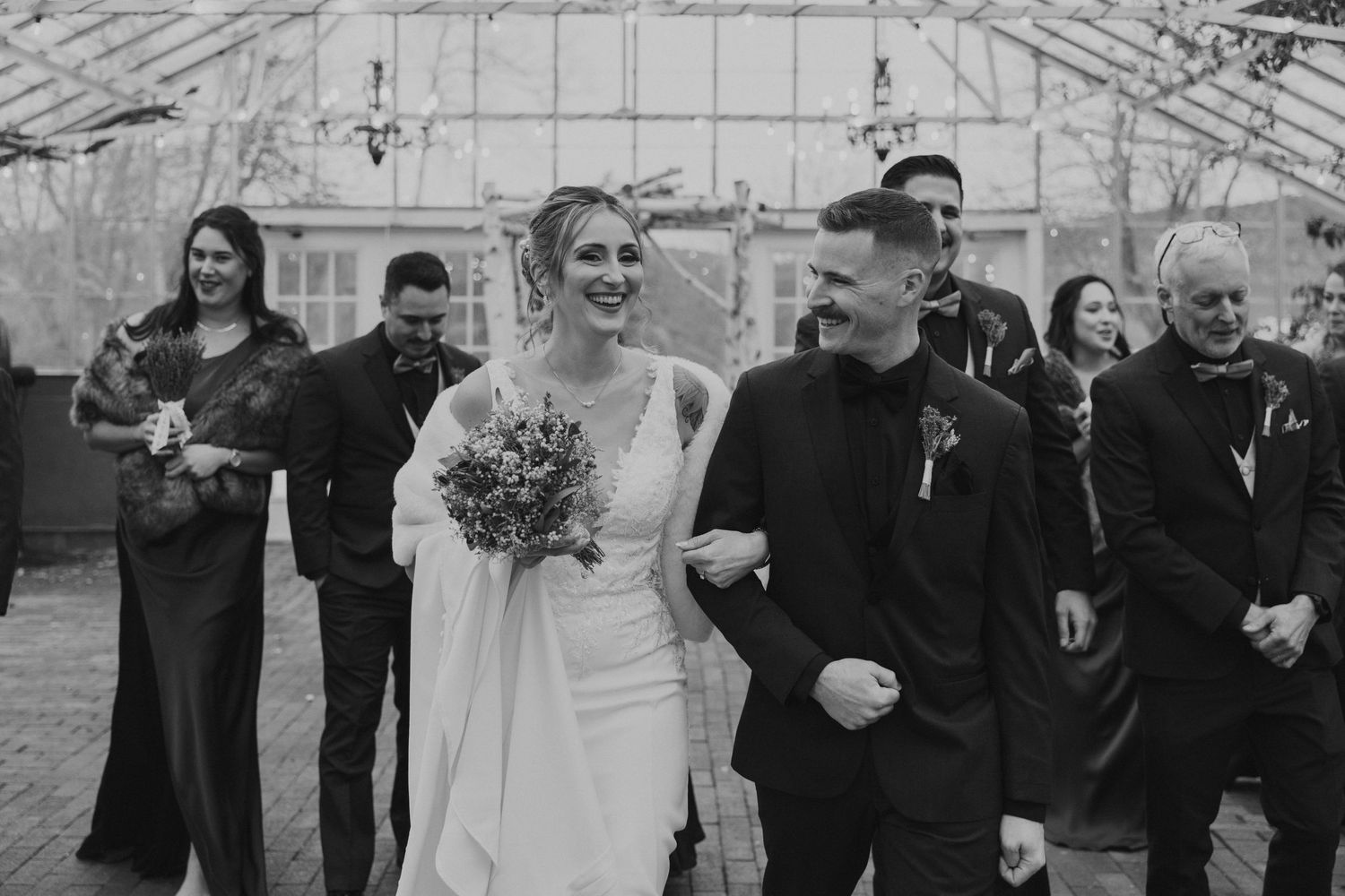 Black and white photo of bride and groom walking joyfully after wedding ceremony.